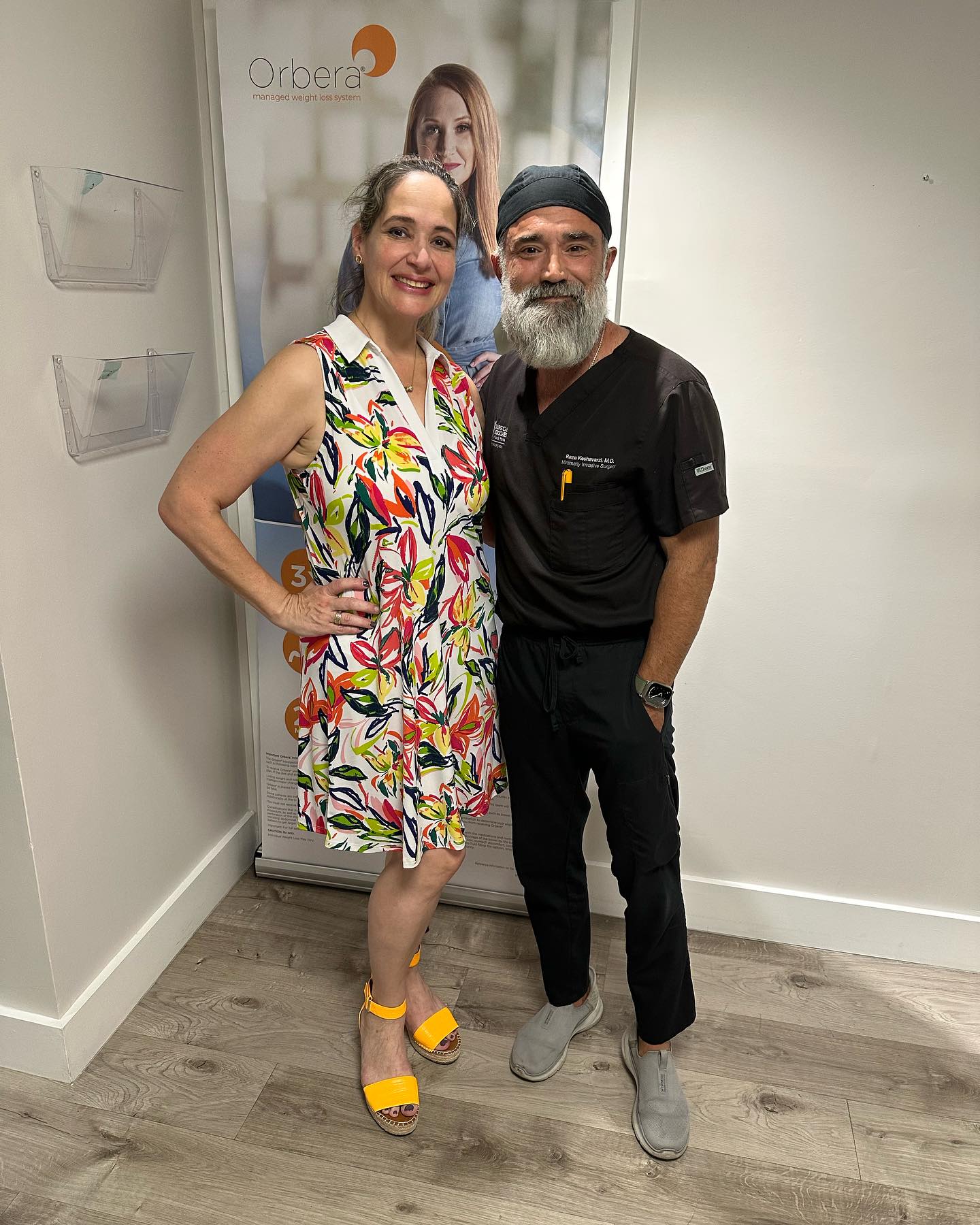 Smiling bariatric surgery patient standing beside Dr. Reza Keshavarzi in the office after her weight loss
