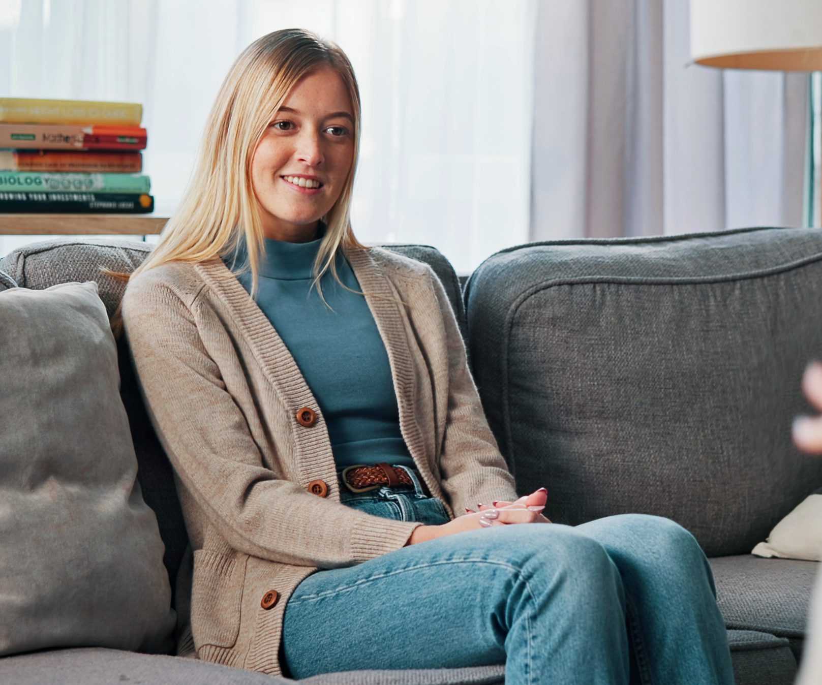 A young woman sits smiling on a couch in a bright living room during what appears to be a therapy or counseling conversation