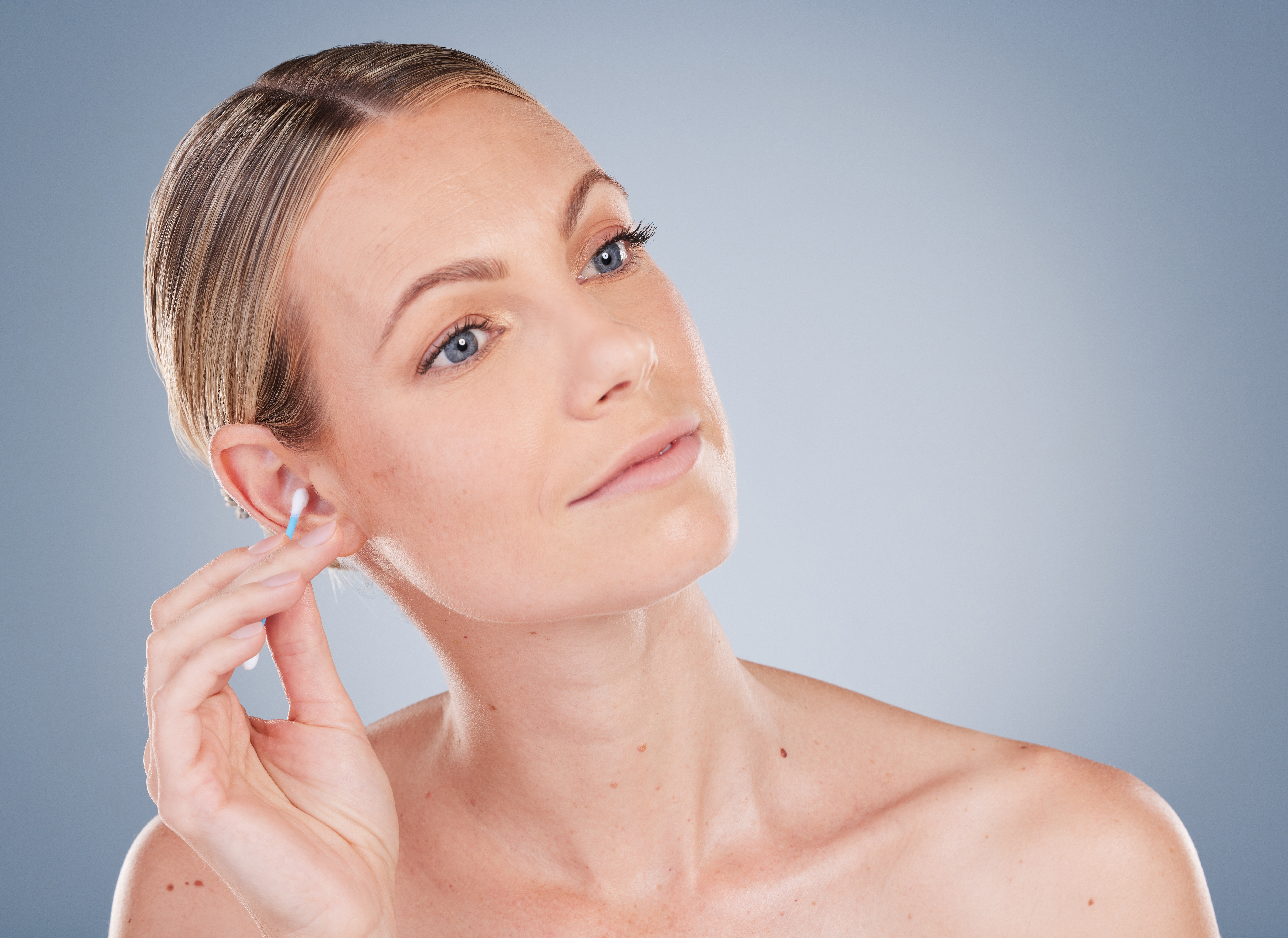 Studio portrait of a woman cleaning her ear with a cotton swab, used to illustrate a blog post about professional ear cleanin