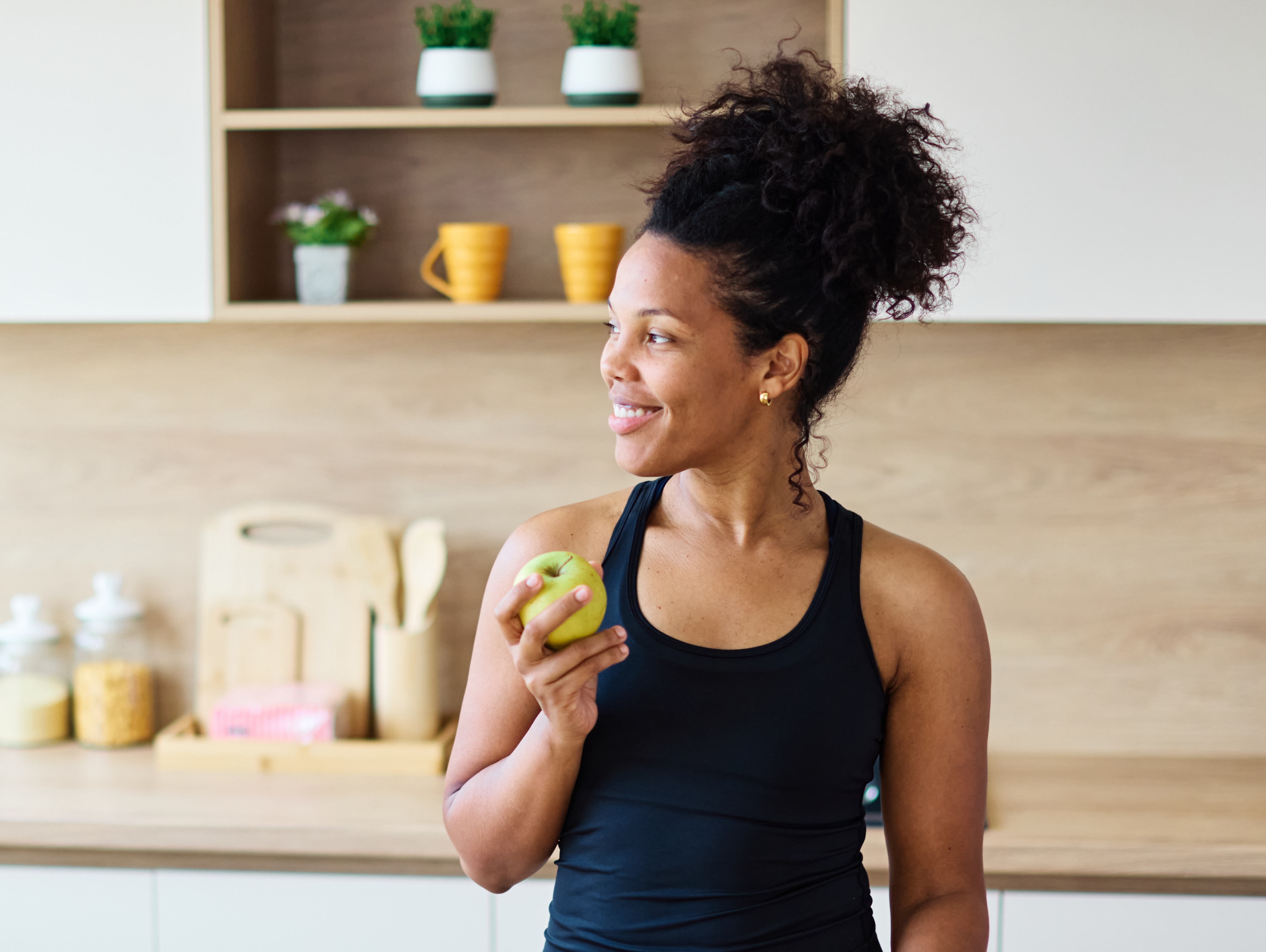 Smiling woman in a bright kitchen holding a green apple as part of a heart-healthy diet