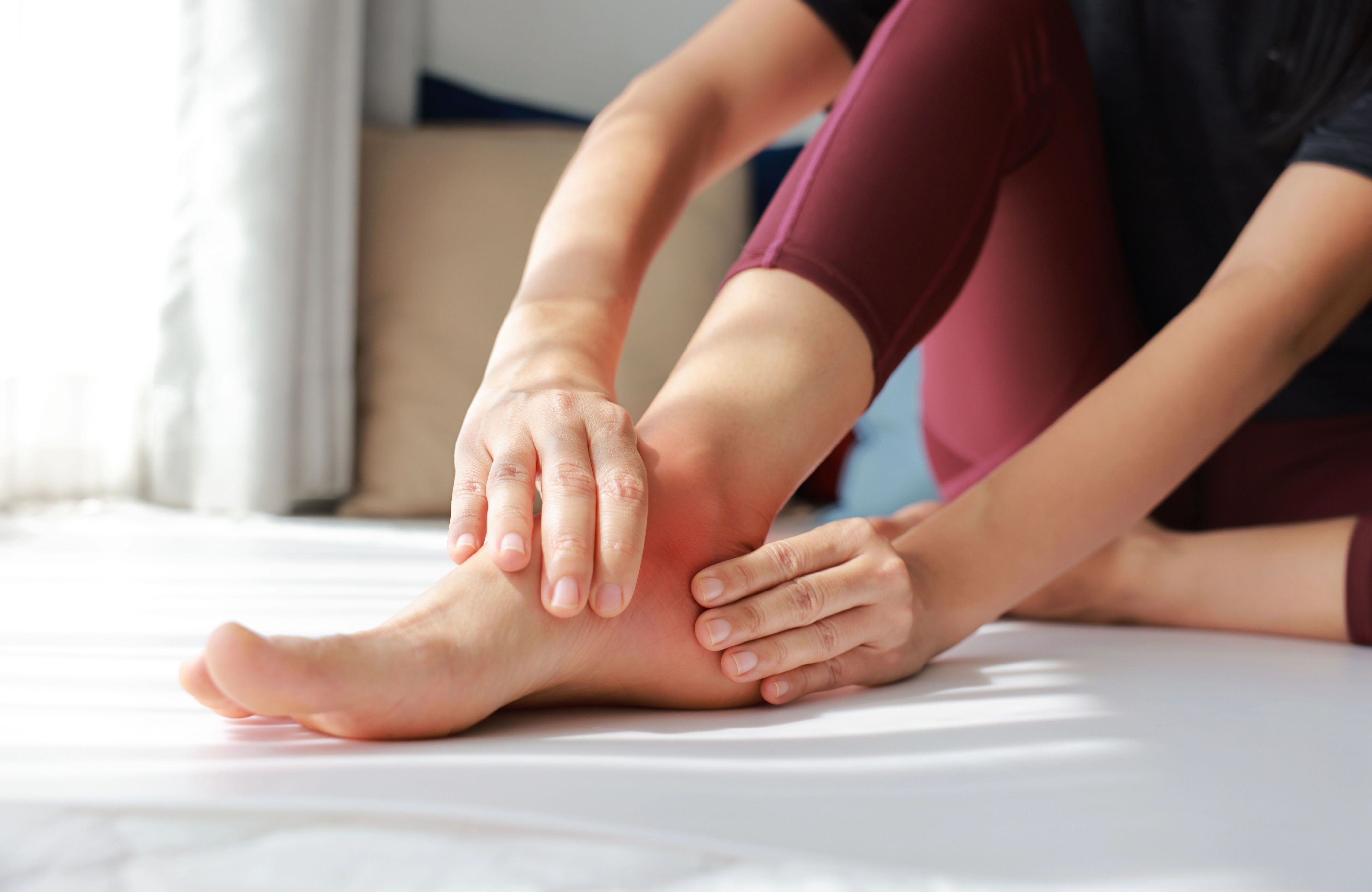 Woman sitting on a bed holding her sore ankle with both hands