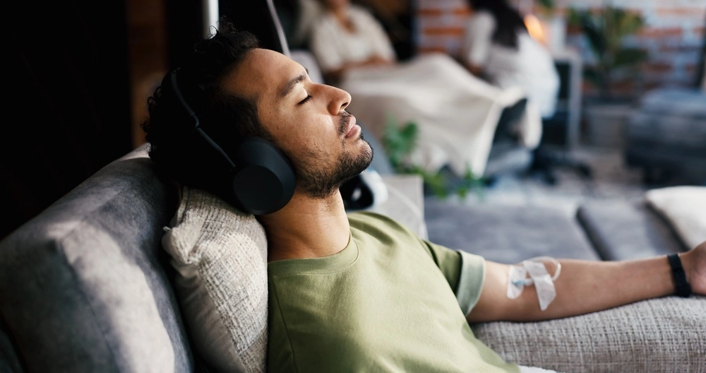 Man resting with headphones on a couch while receiving an IV infusion