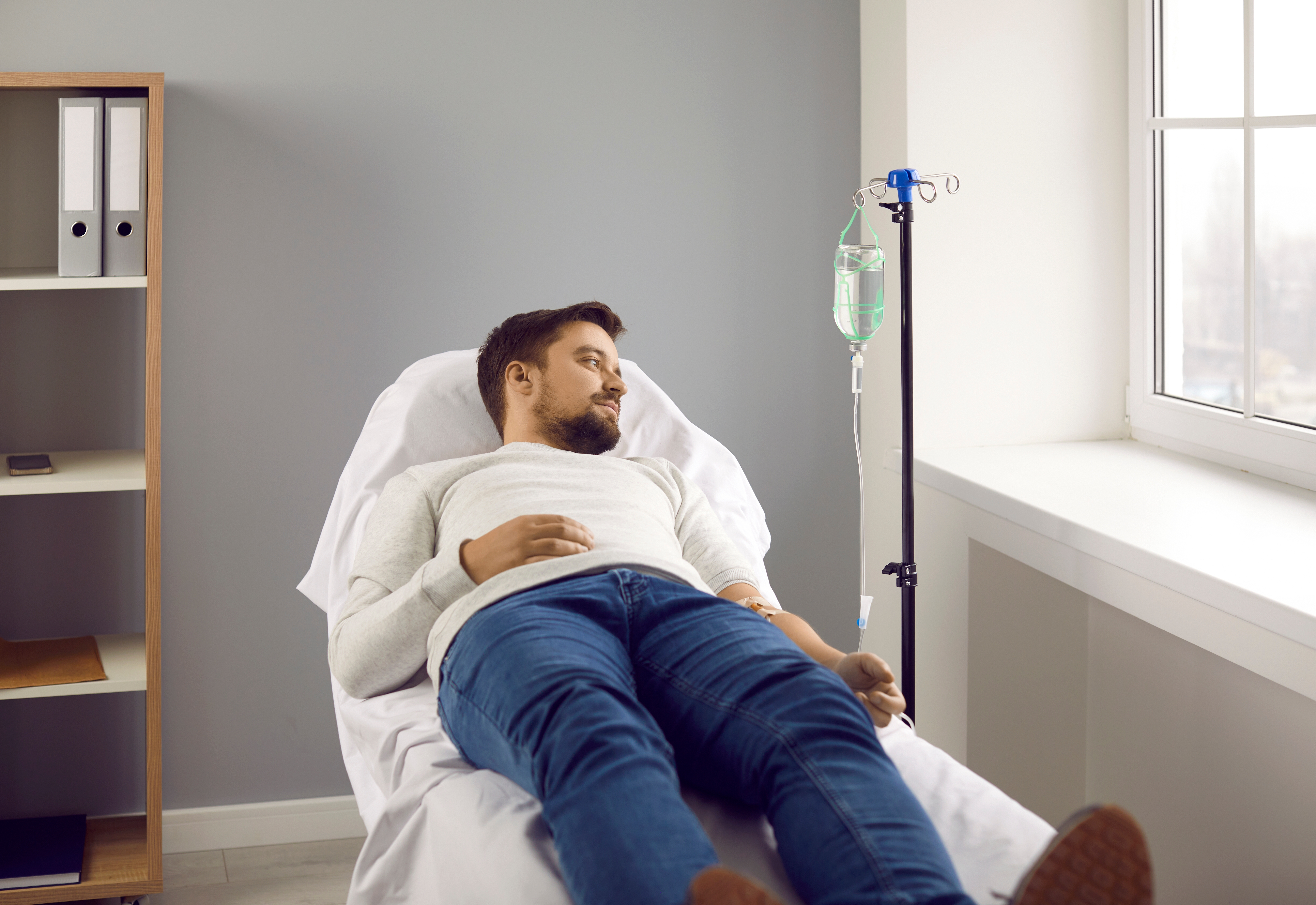 A man reclines in a chair receiving an IV infusion therapy near a sunlit window