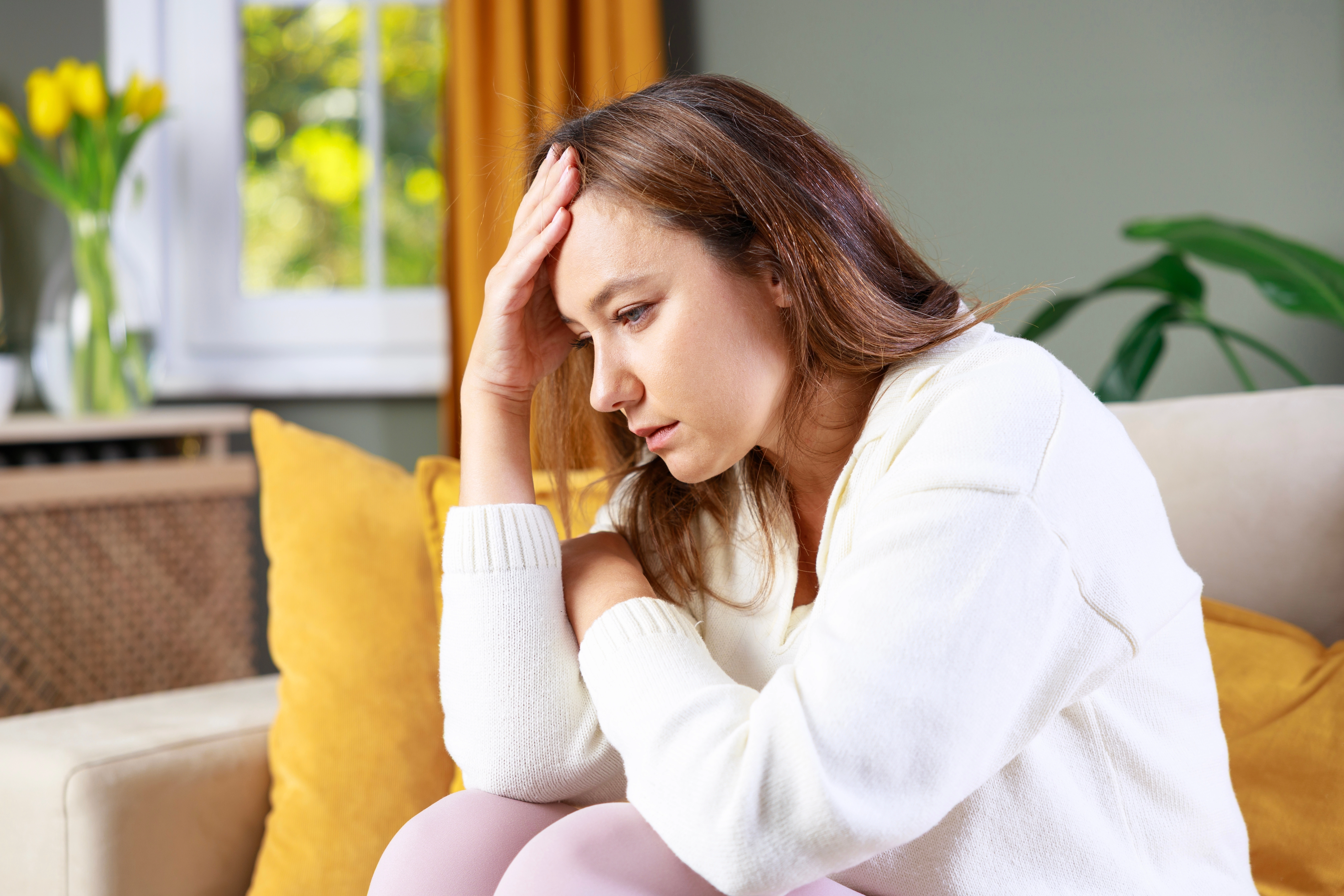 A woman sits on a couch holding her head in distress, illustrating the concept of anxiety for a blog post about the differenc