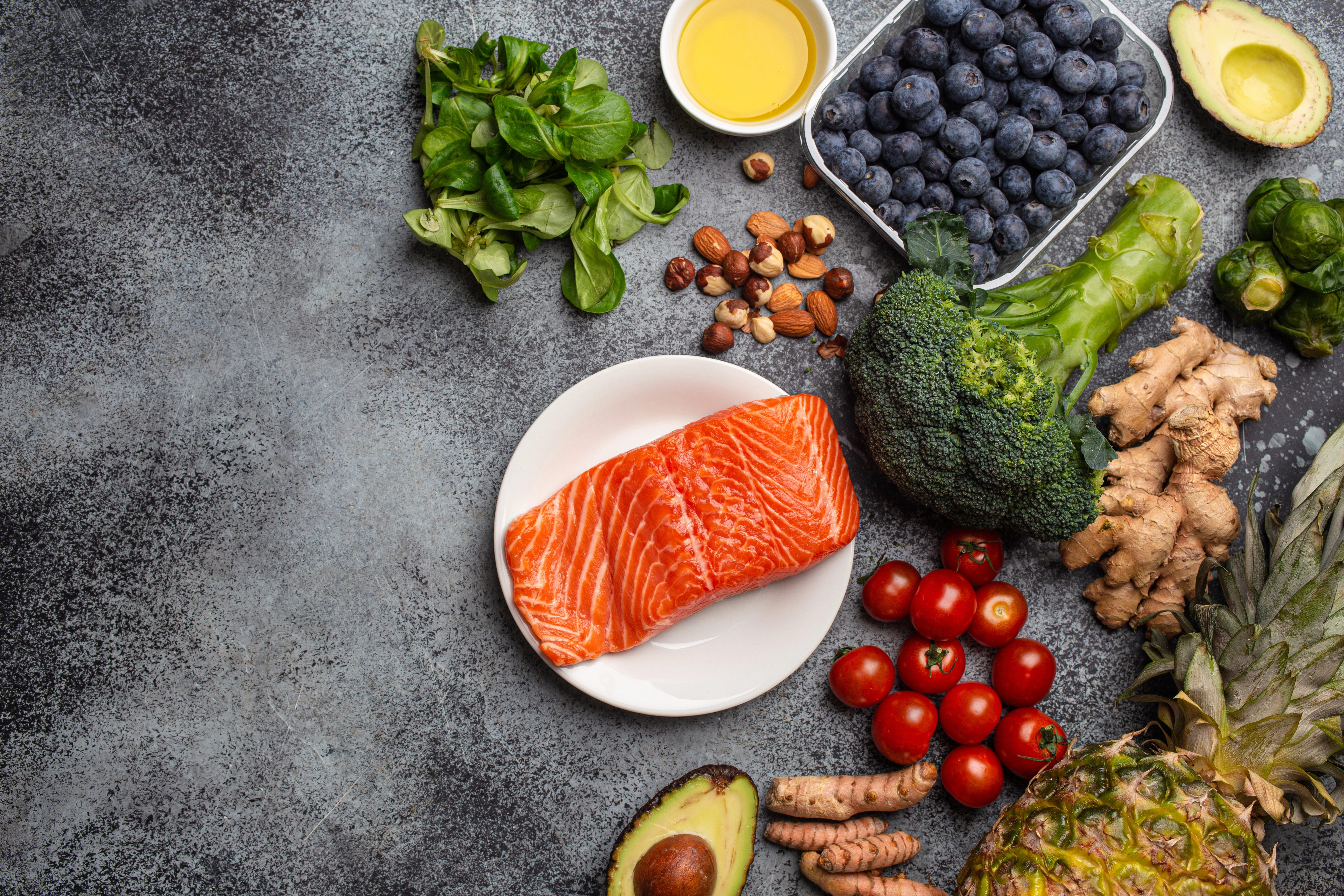 Salmon fillet, avocado, blueberries, broccoli and nuts laid out on a dark stone surface