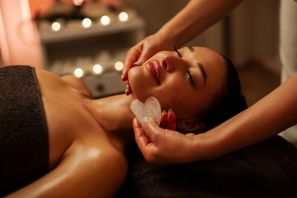 A relaxed woman receives a gua sha facial treatment during a candlelit spa session