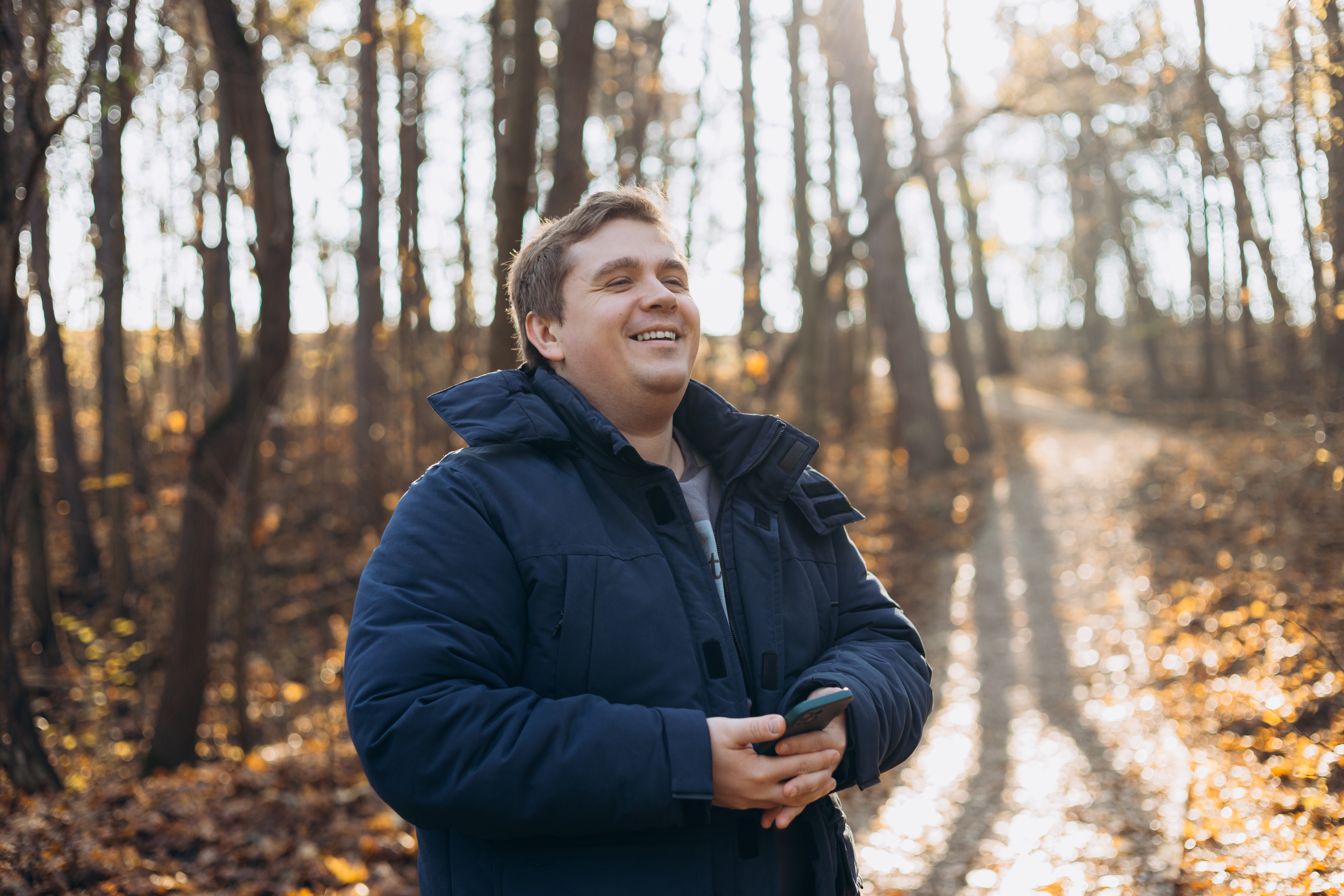 Smiling man in a winter coat on a sunlit forest trail