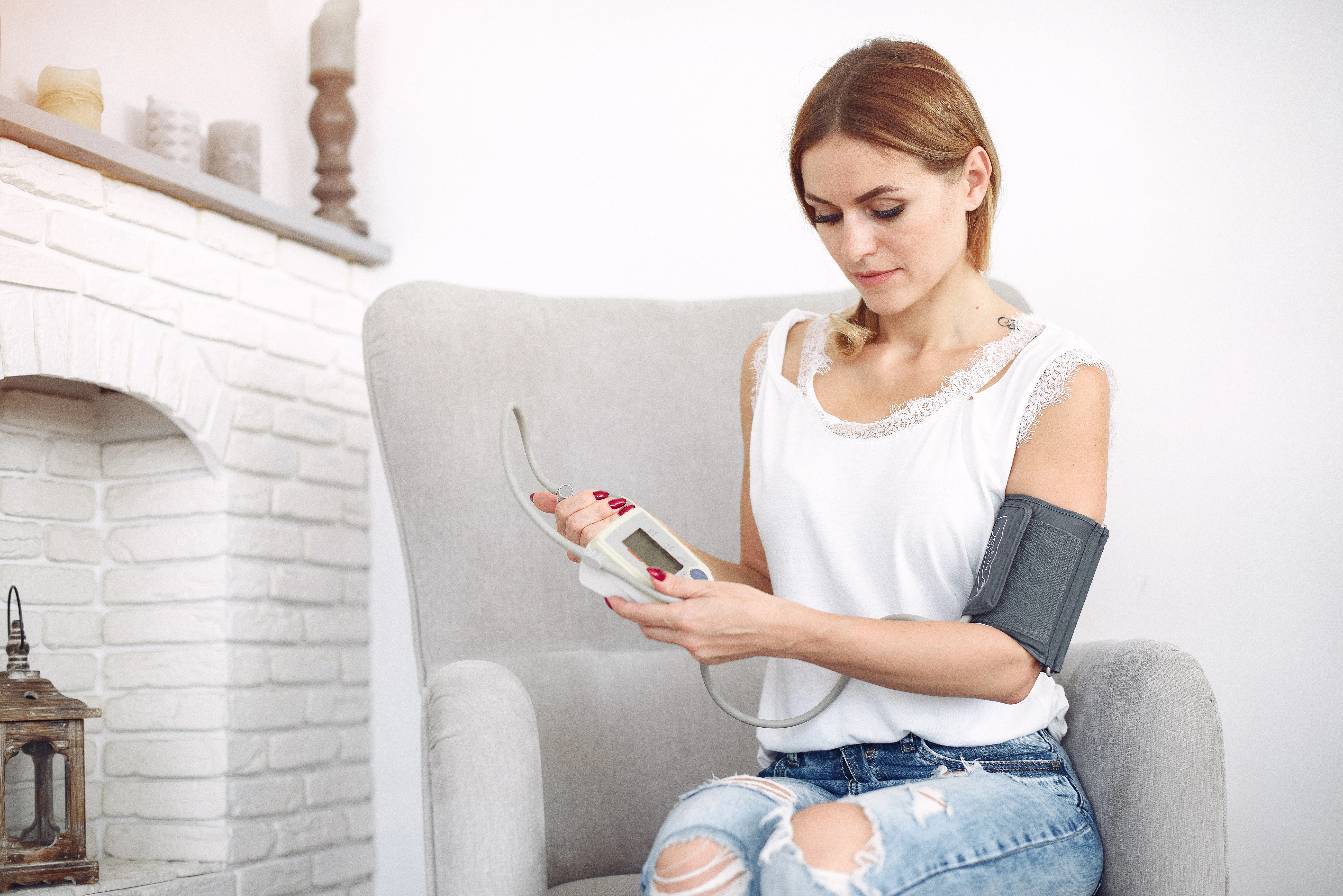 Woman seated in an armchair at home checking her blood pressure with an arm cuff monitor