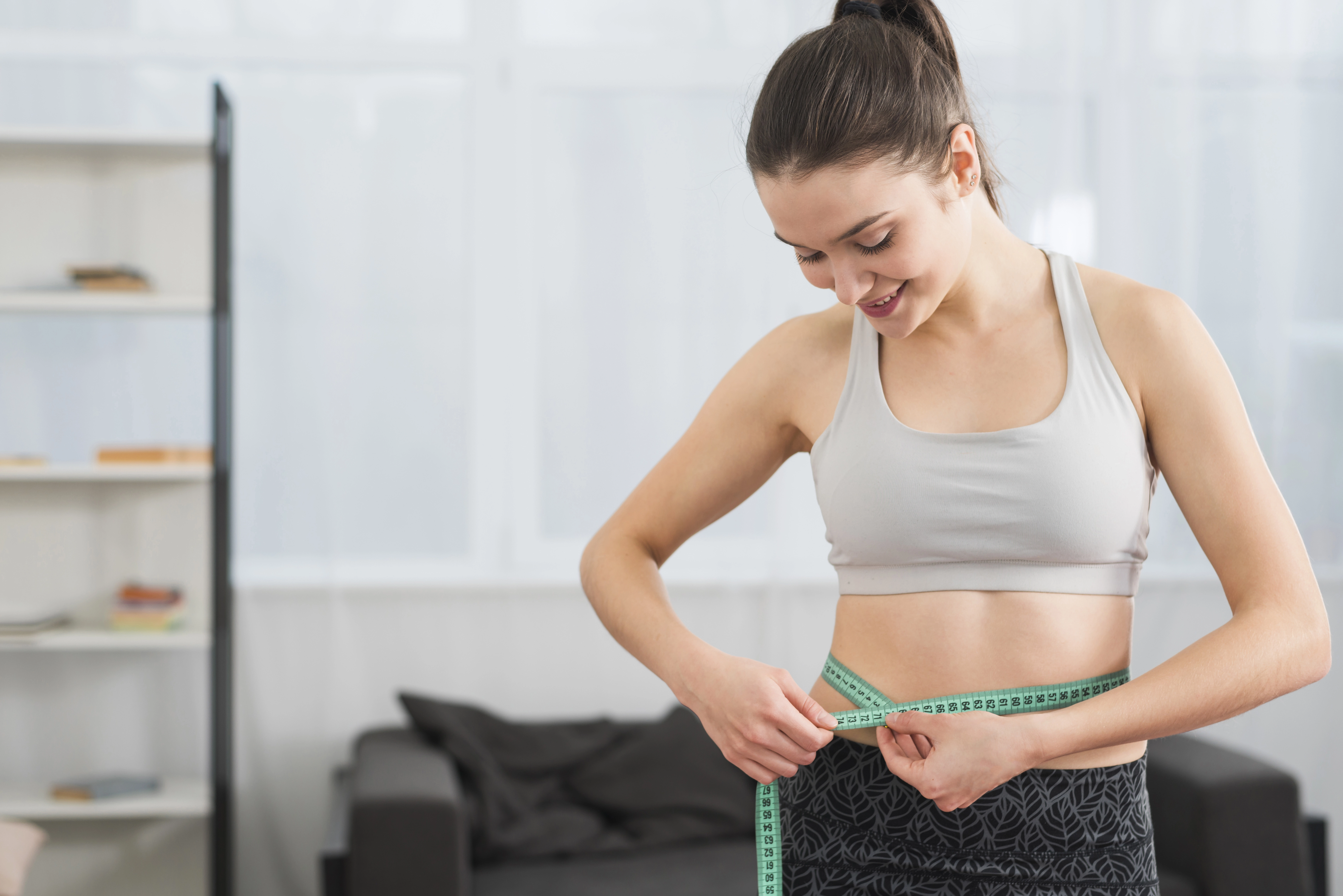Smiling woman in athletic wear measuring her waist with a tape measure to track progress