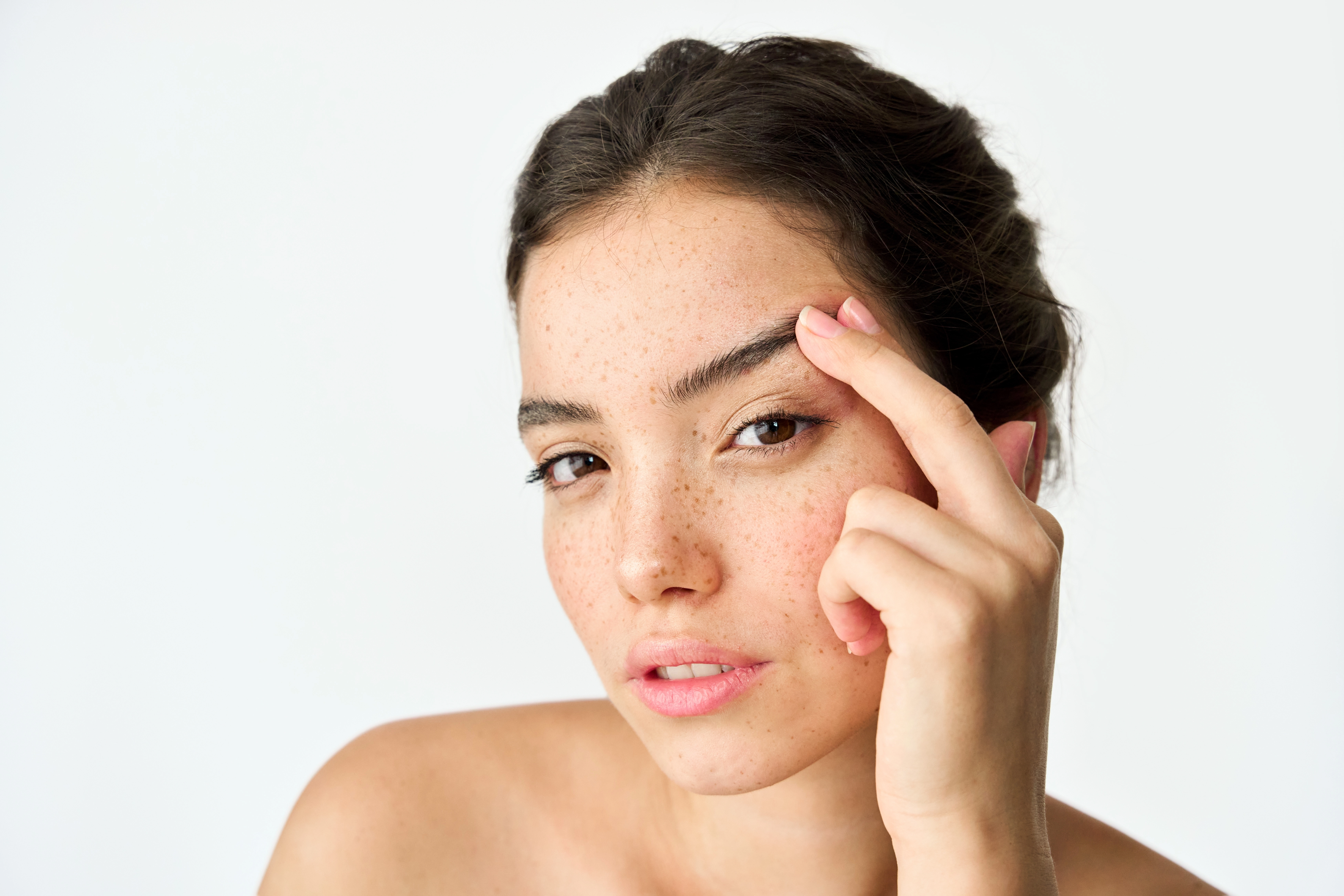 Close-up studio portrait of a woman touching her brow area to showcase natural skin texture and freckles