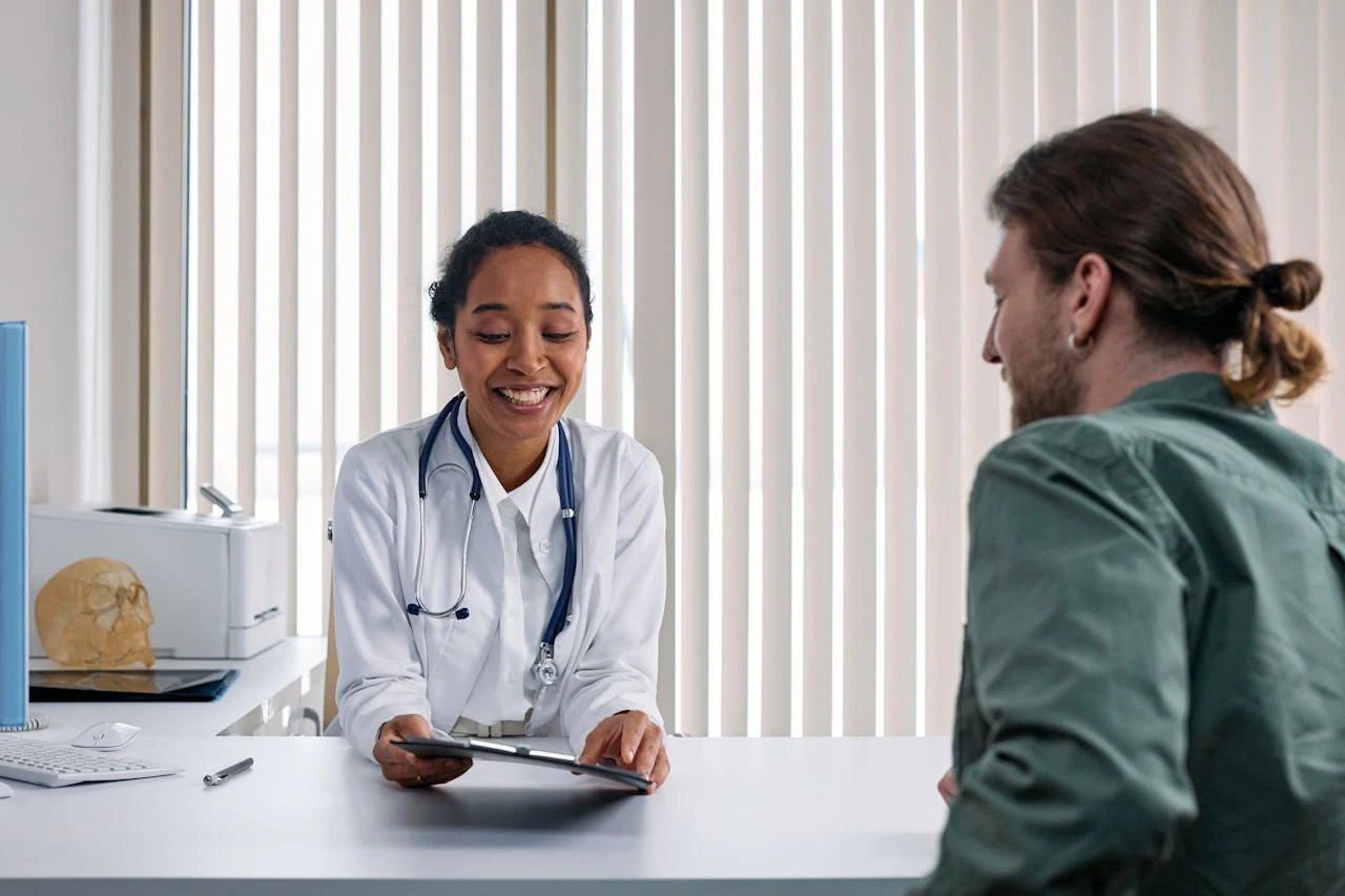 A smiling female doctor in a white coat reviews information on a tablet with a male patient during a consultation.