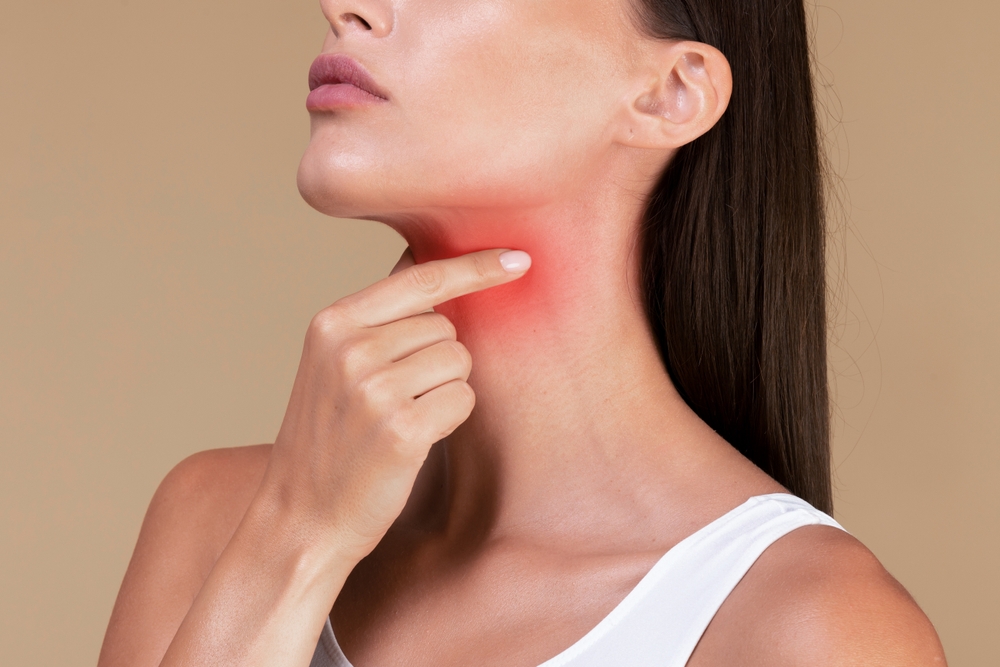 A woman touches her throat with a highlighted red area indicating throat or thyroid pain