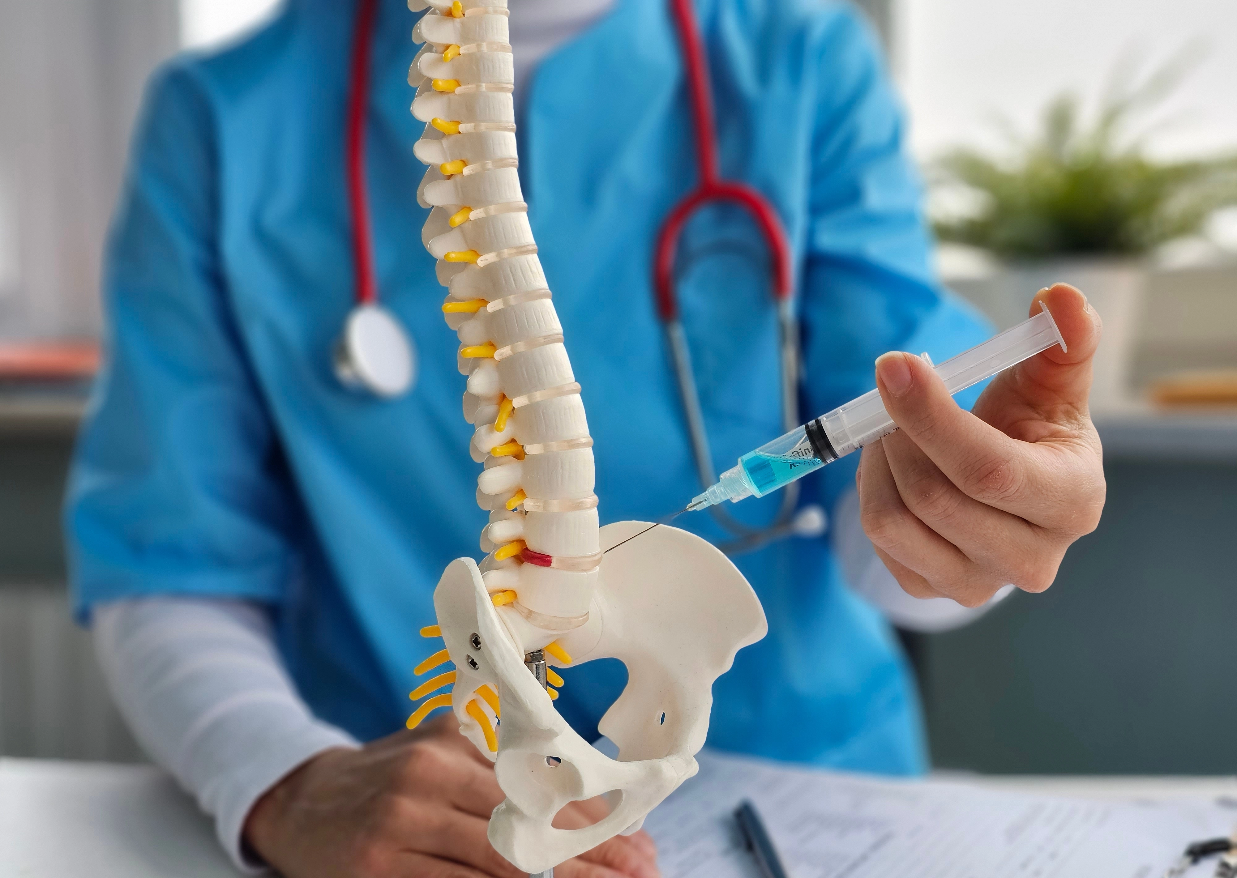 Clinician holding a syringe beside an anatomical model of the spine and pelvis