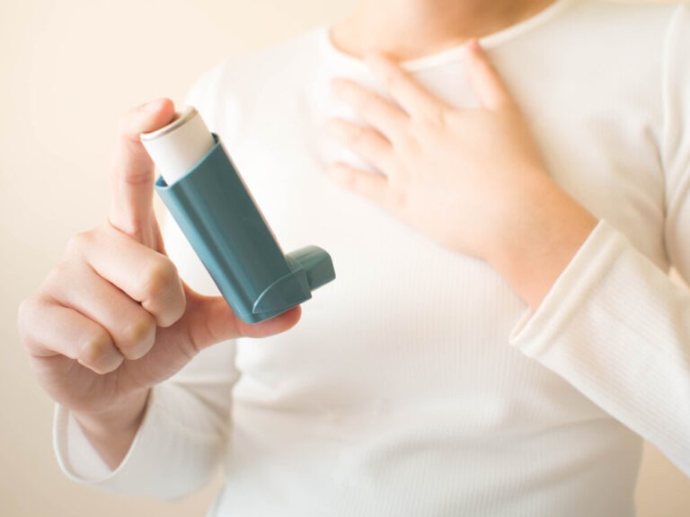 Cropped photo of a woman holding an inhaler to her chest, illustrating asthma symptom management
