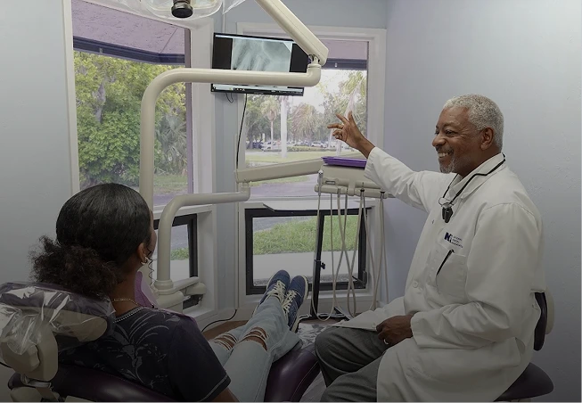 Image: A dentist pointing to a dental X-ray on a screen while explaining to a patient where the biting pain is coming from.