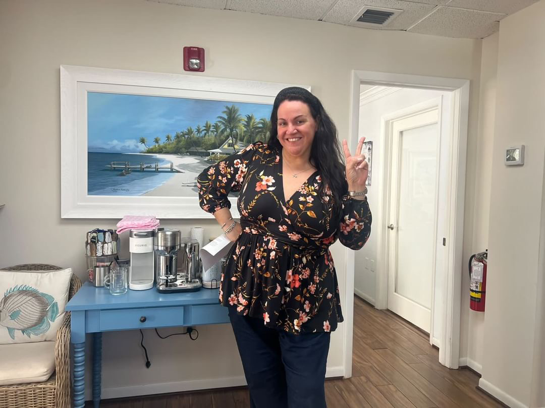 A smiling patient in a floral blouse celebrating her weight loss milestone in our office hallway