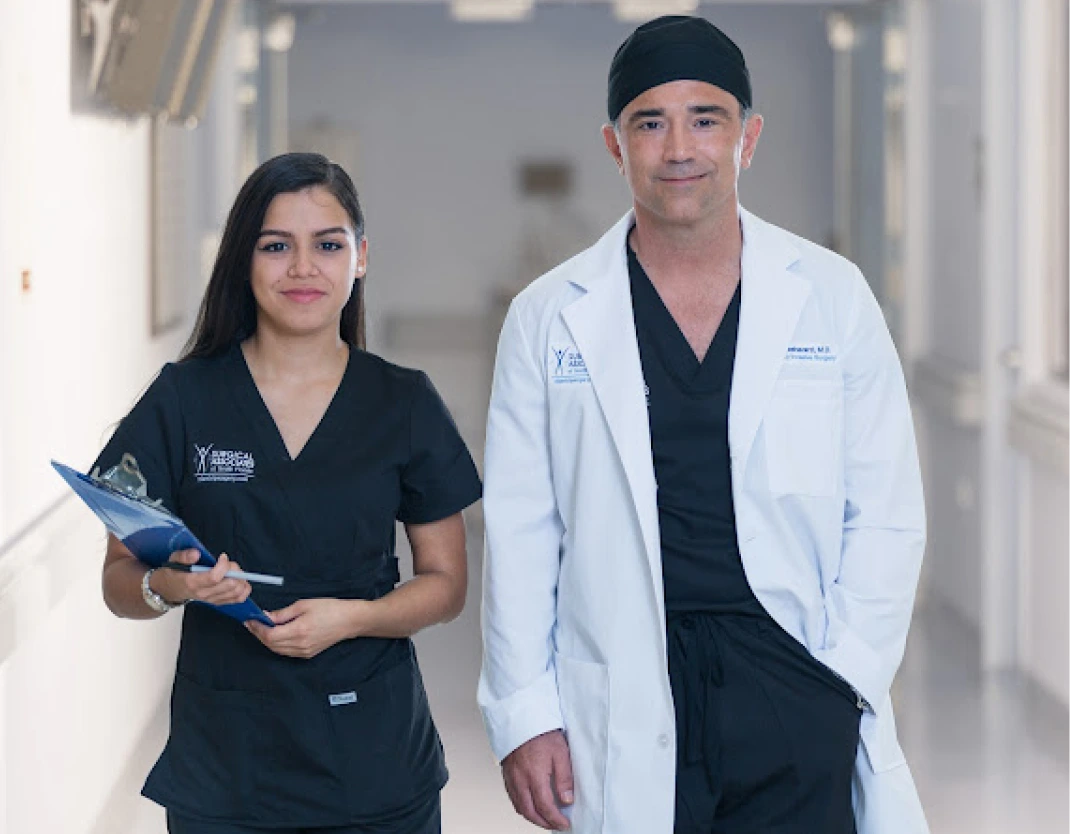 Dr. Reza Keshavarzi in a white coat and a team member in branded scrubs standing in a bright hallway