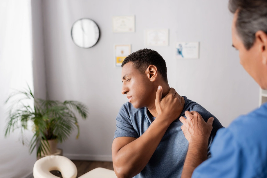 A male patient winces while a provider examines his neck and shoulder in a clinical office setting