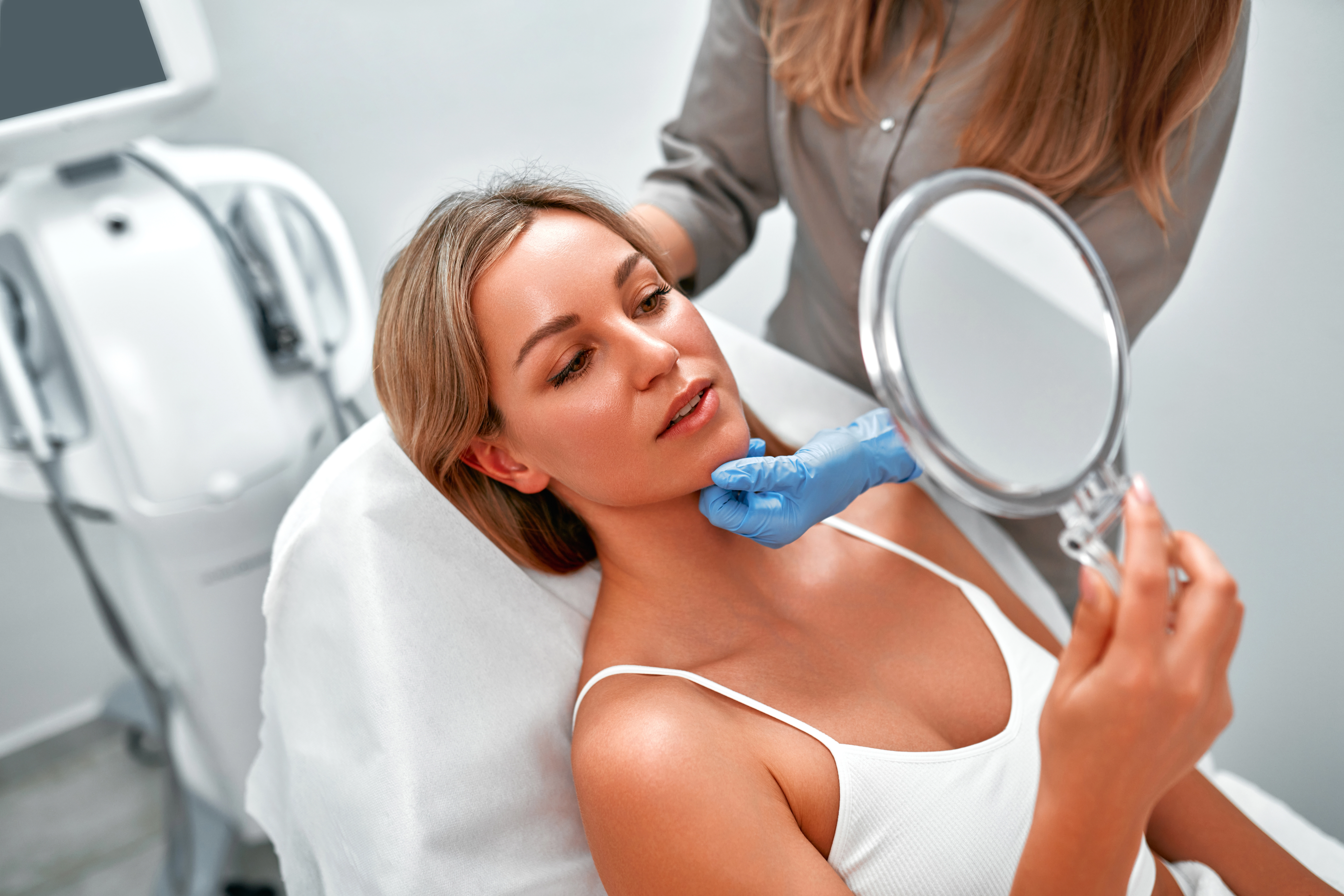 A provider gently assesses a patient's chin and jawline while she looks in a hand mirror