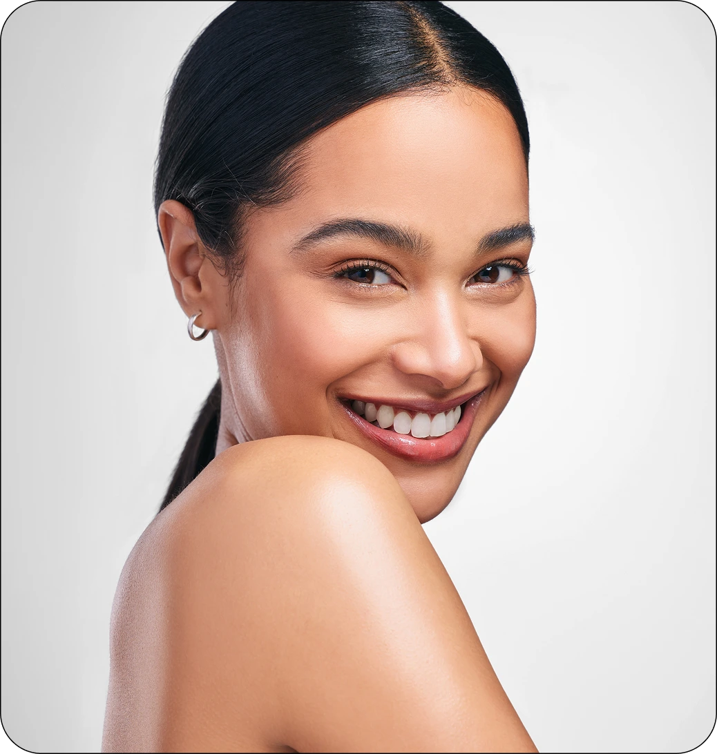 Smiling woman with glowing skin and sleek dark hair looking back over her bare shoulder