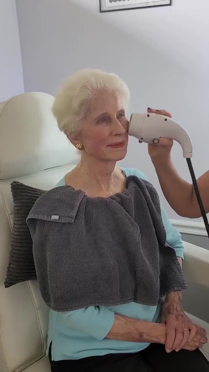 An older woman relaxing in a treatment chair while a handheld device lifts the skin of her cheek and temple at Anti Aging Center of Boca