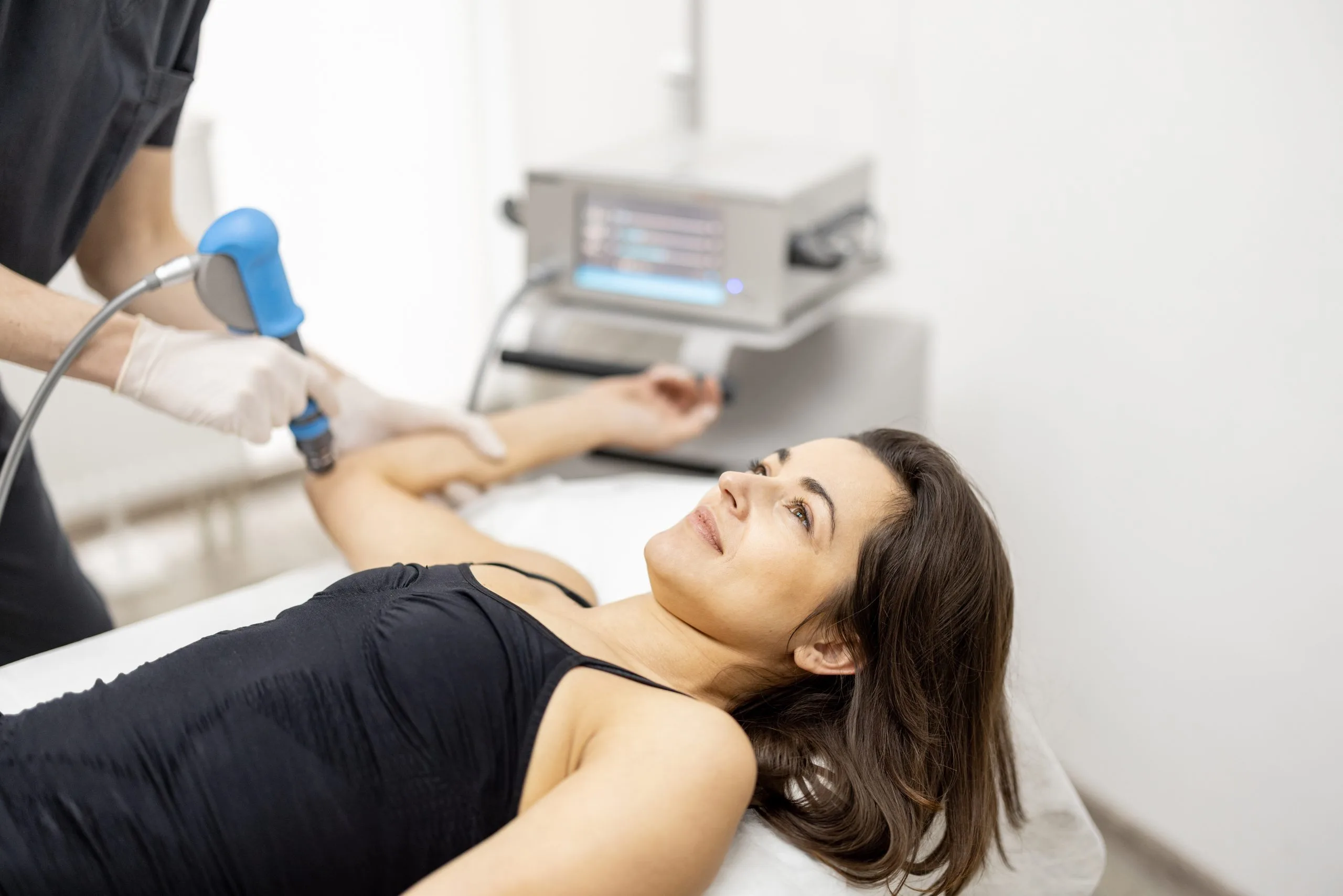 Clinician using a blue handheld ultrasound probe on a patient's arm during a treatment session