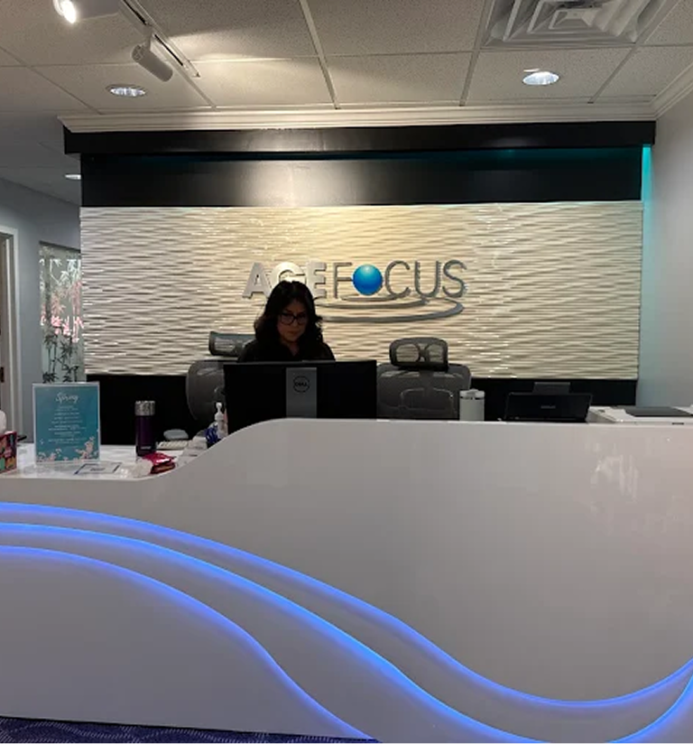 Reception desk at AcueFocus clinic with staff member seated behind counter and illuminated blue wave design in foreground
