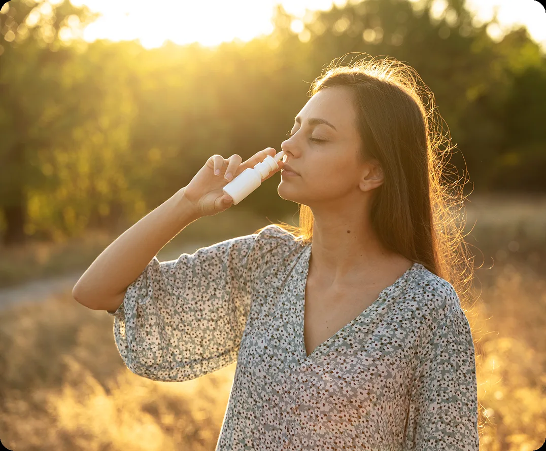 Woman using a nasal spray outdoors in golden sunlight