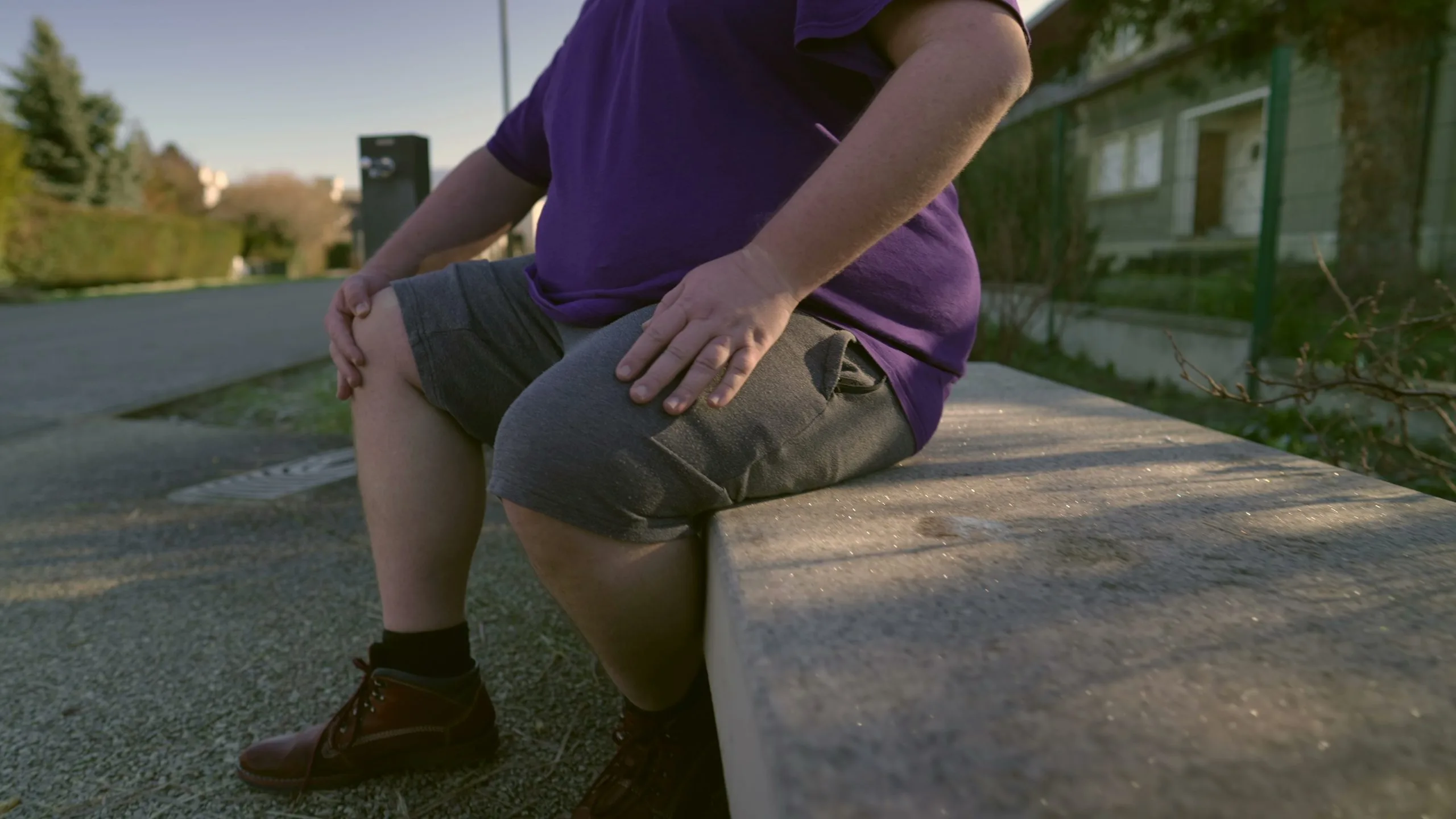 Child sitting on a concrete ledge wearing a purple shirt and gray shorts.