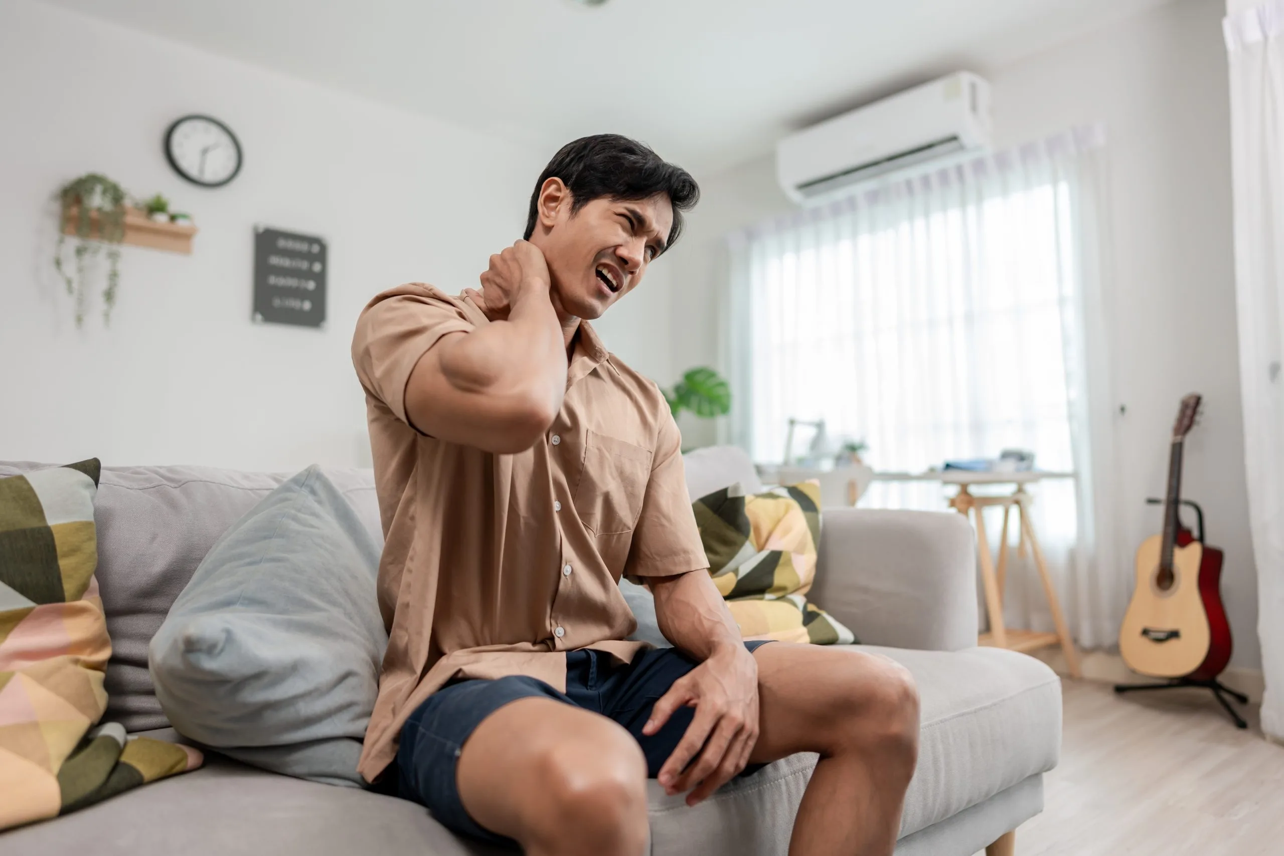 Man sitting on couch holding his neck in pain.