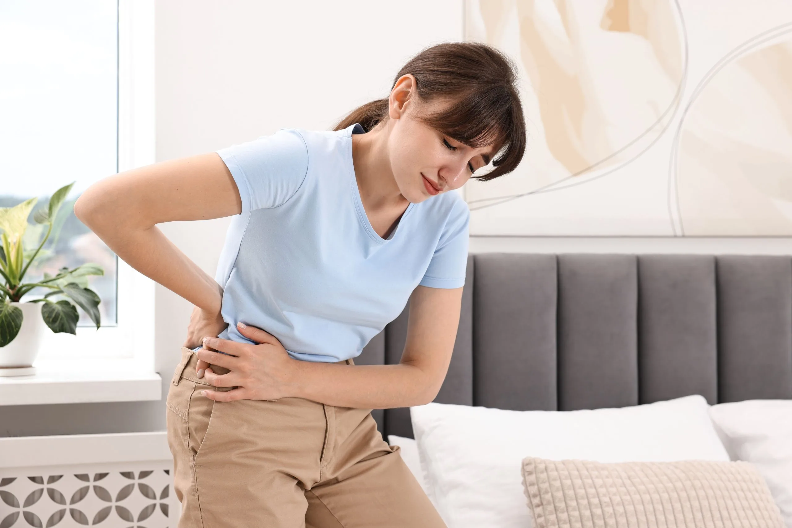 Woman in white t-shirt holding lower abdomen in pain while sitting on bed