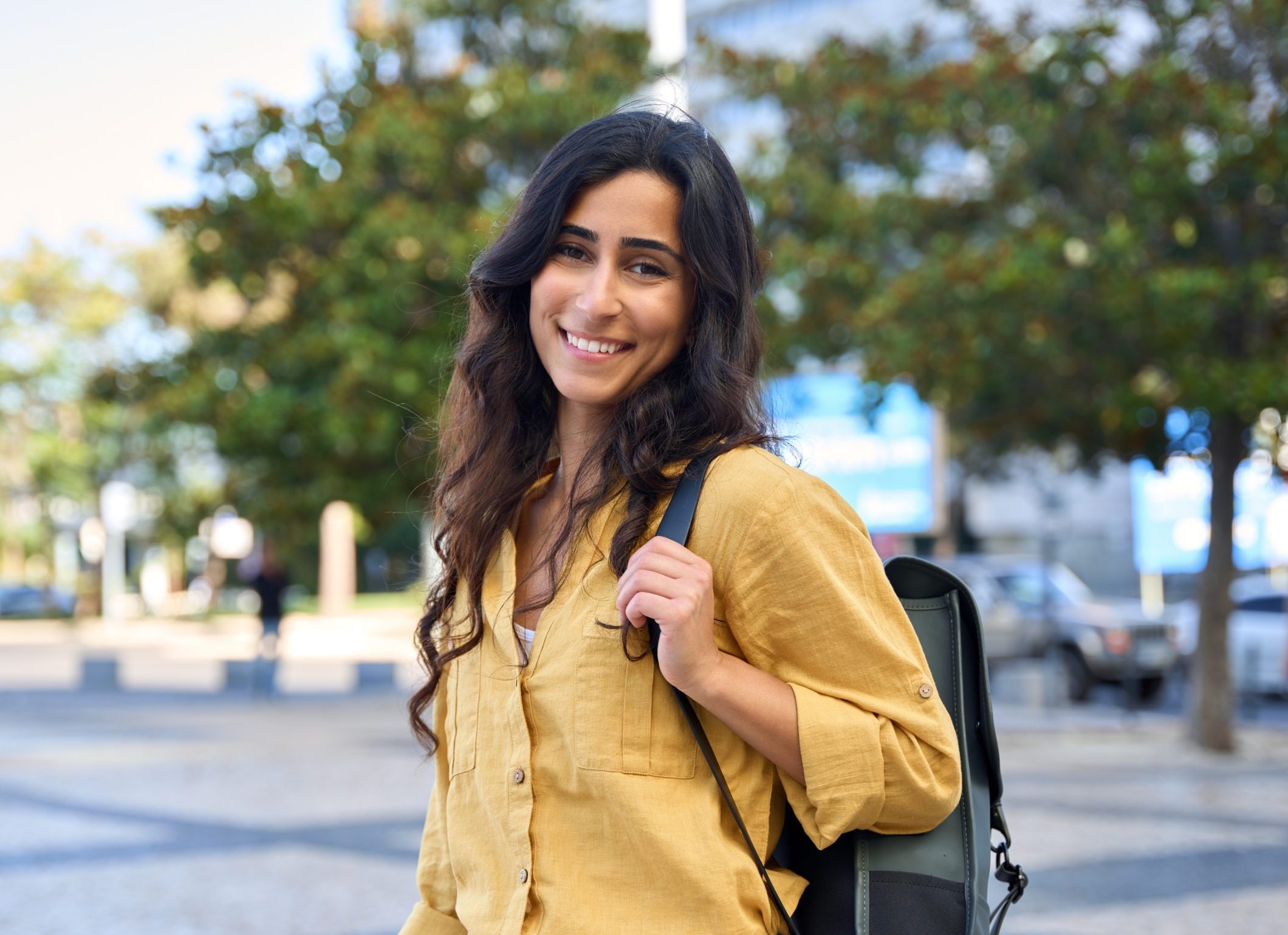 Smiling young woman wearing a yellow shirt and backpack outdoors
