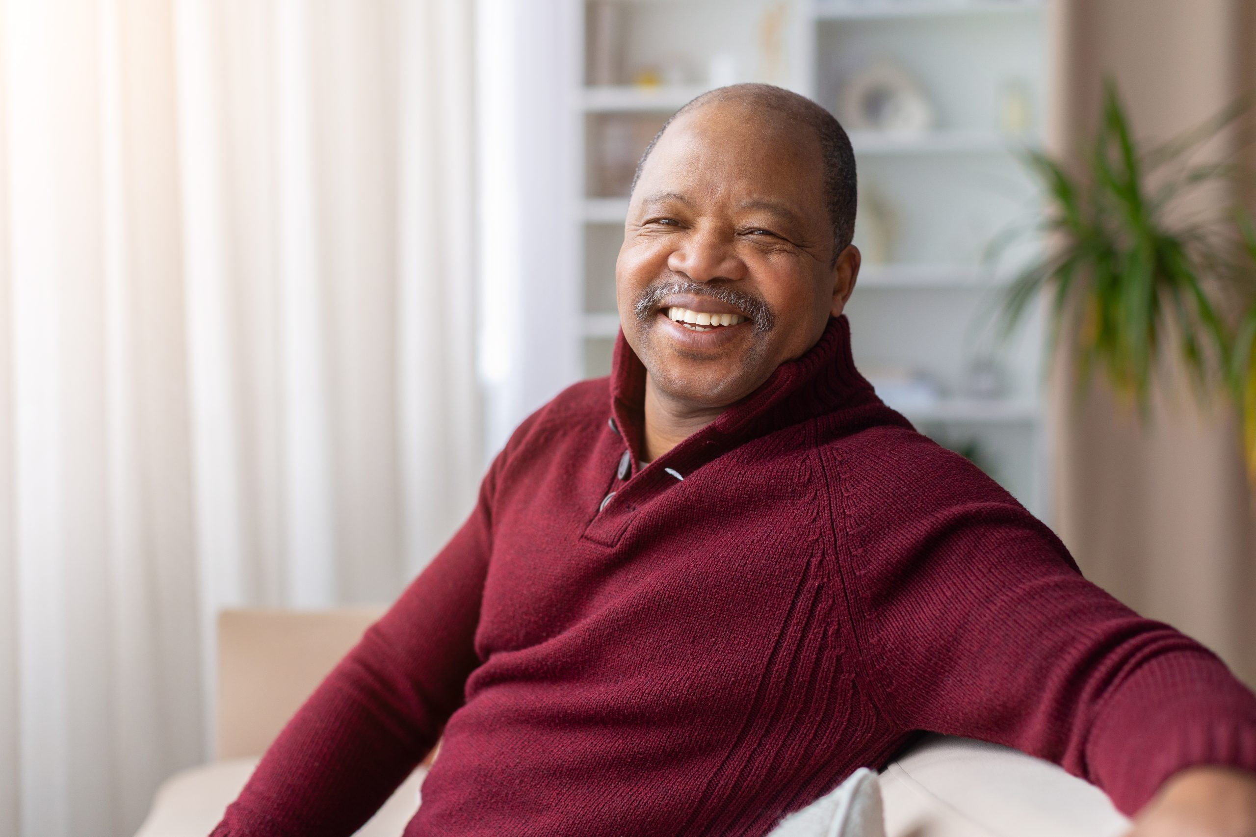 Smiling mature man relaxing on sofa at home in burgundy sweater
