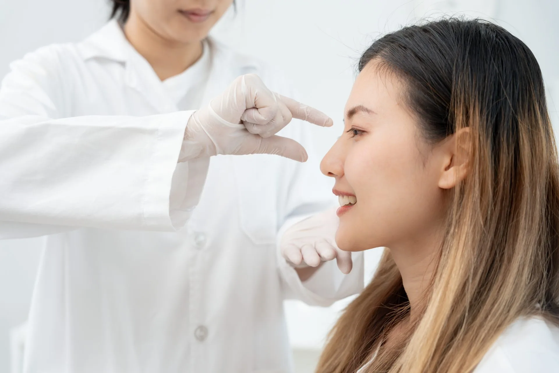 Clinician in white coat measuring patient's nose profile with calipers