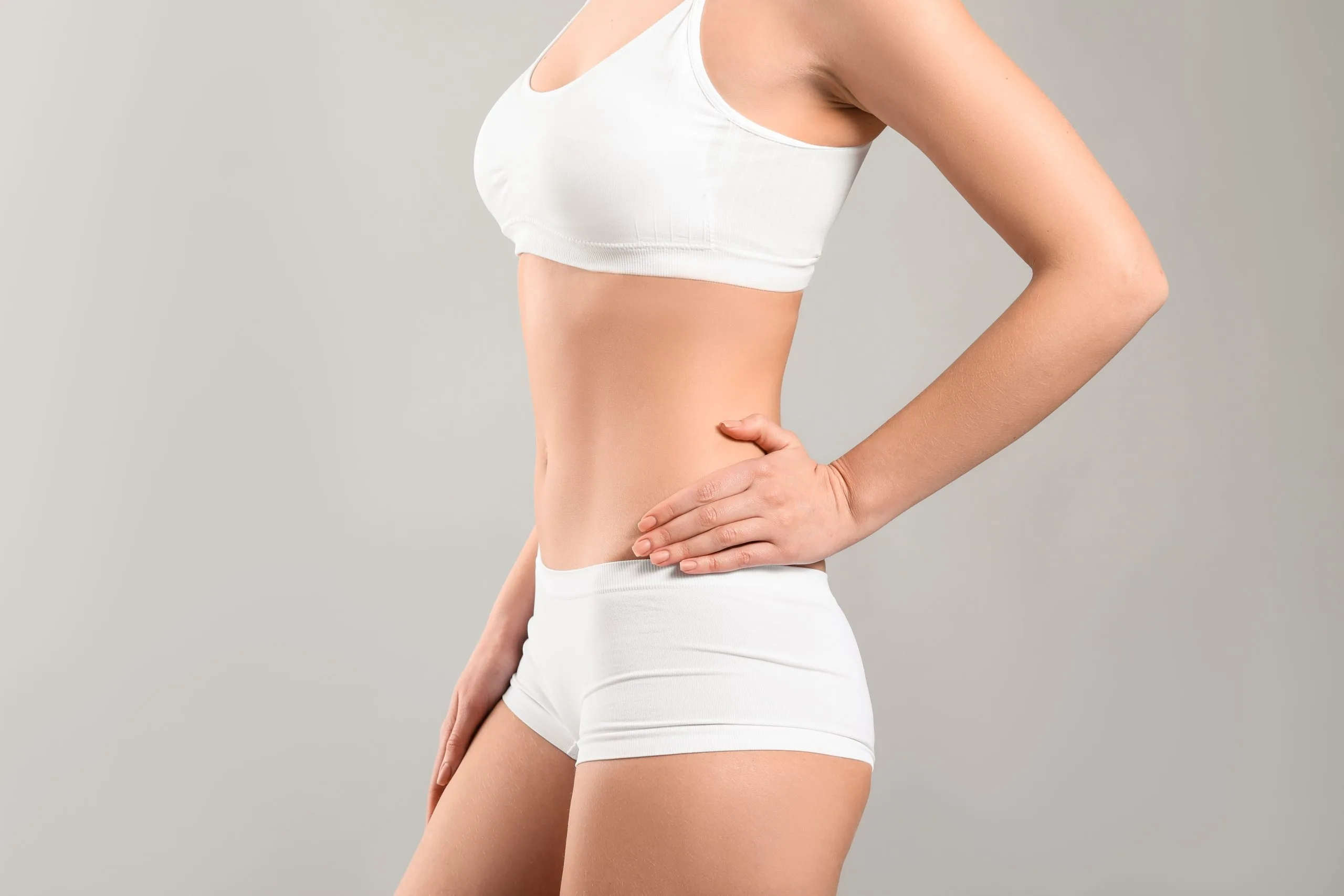 Woman in white undergarments touching her abdomen against a grey background