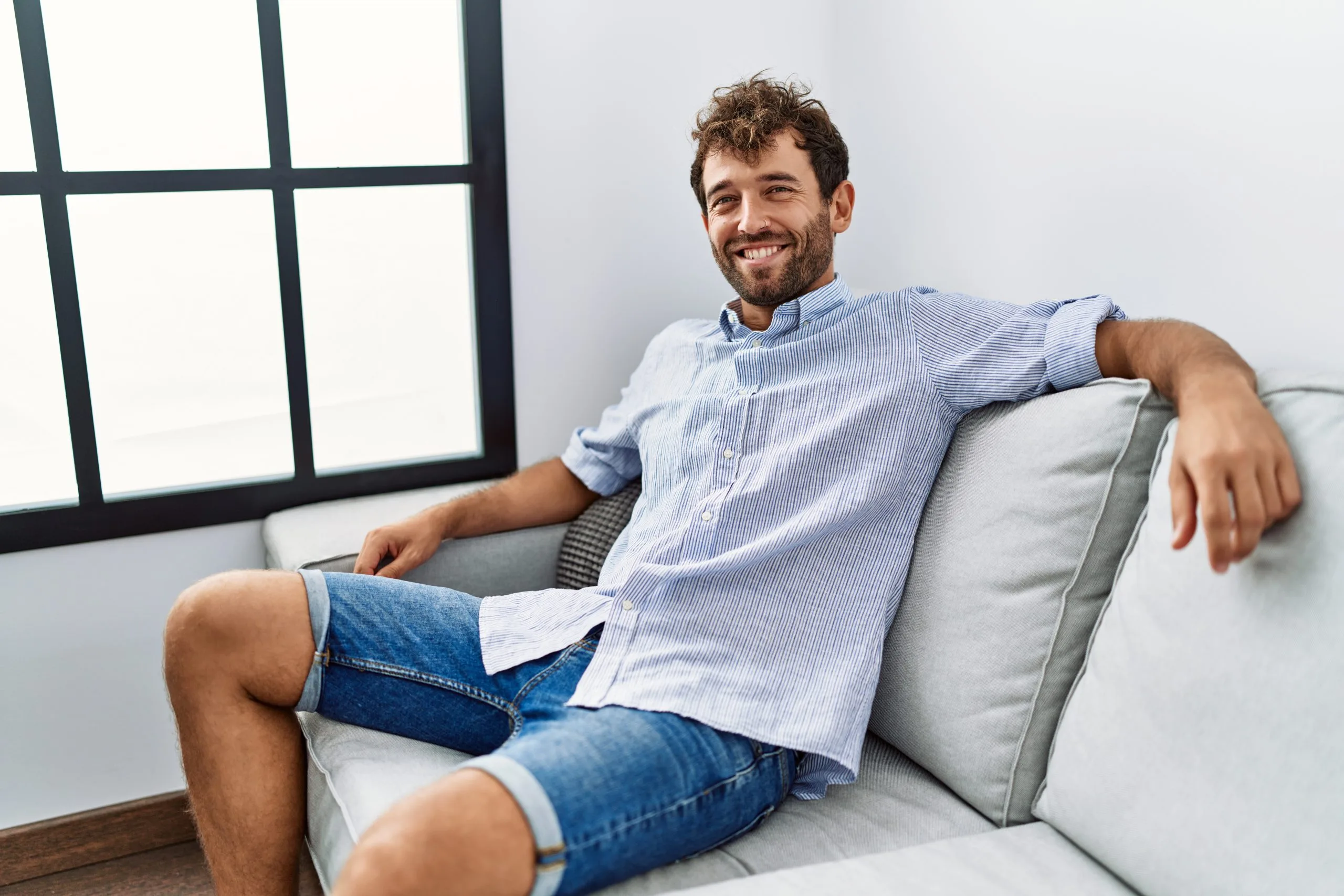 Man relaxing on a couch in a bright room with large windows