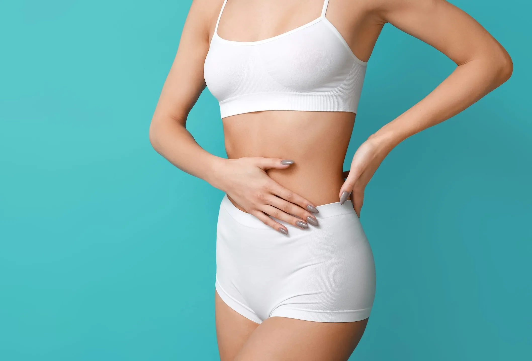 Woman in white undergarments touching her lower abdomen against a turquoise background