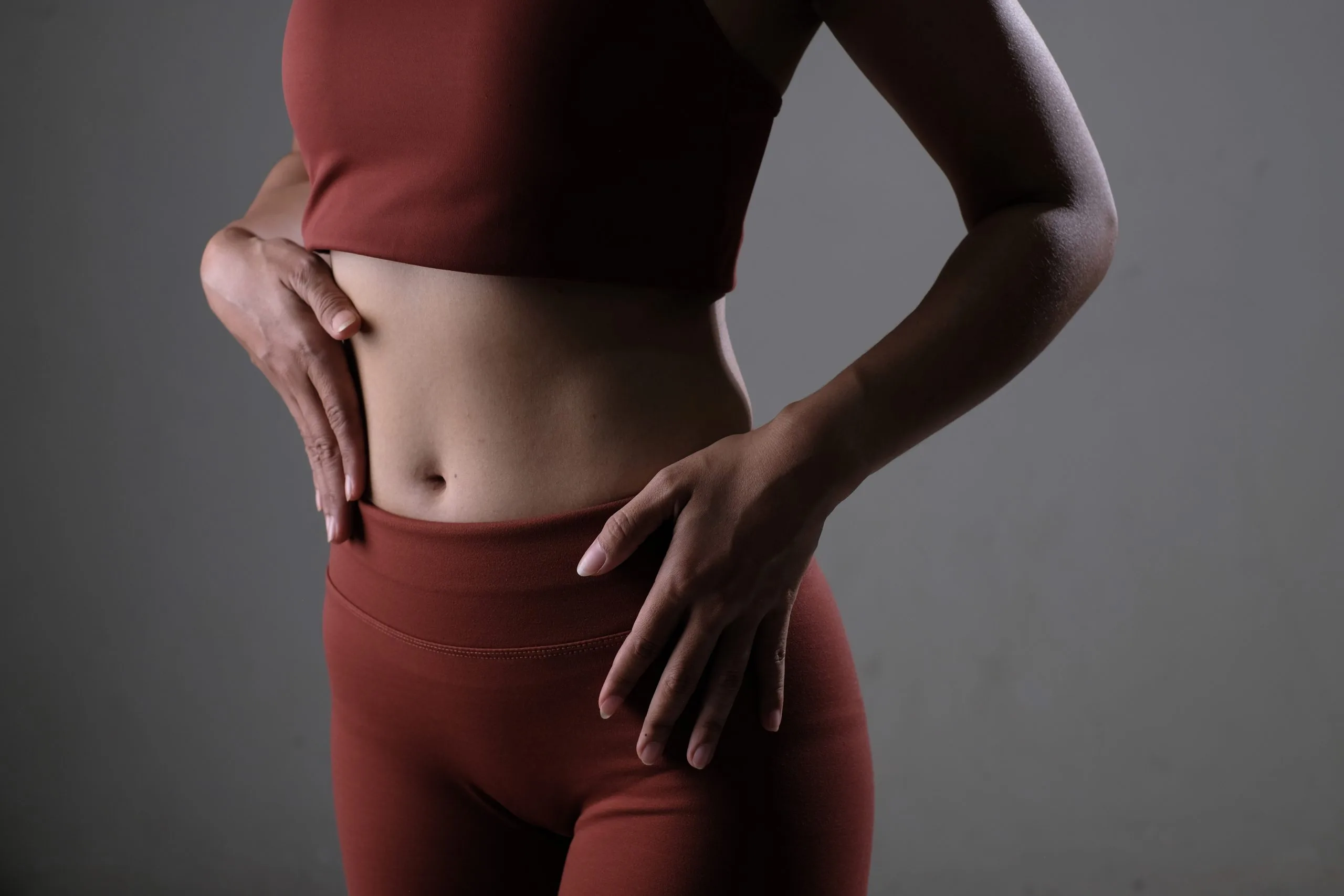 Confident woman in burgundy workout clothes posing to show toned abdominal and hip contours