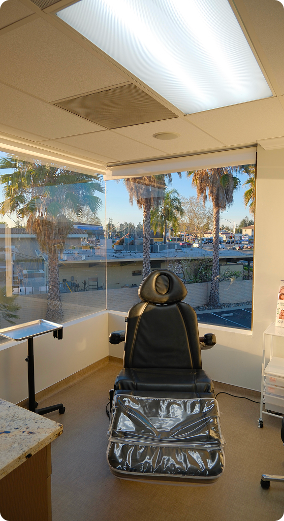 Medical treatment room with black procedure chair and windows overlooking palm trees
