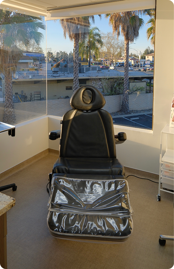 Black treatment chair with footrest in bright med spa treatment room overlooking palm trees
