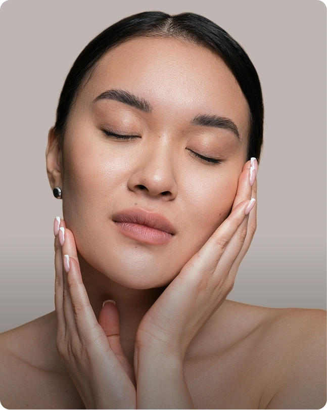 Woman with eyes closed touching her face demonstrating skin treatment results