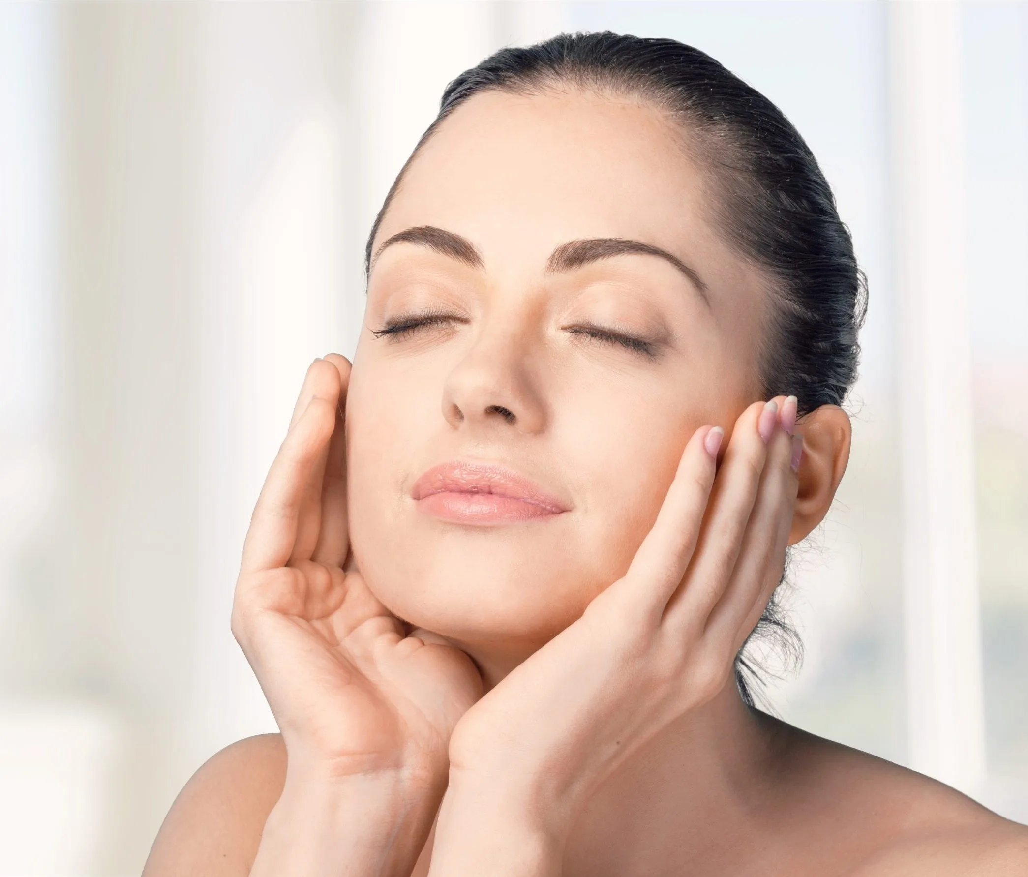 Woman with eyes closed cradling her face with both hands against a neutral background