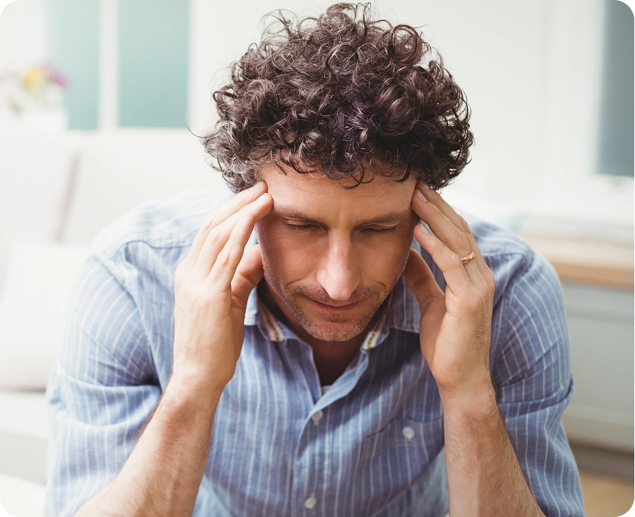 Man in blue striped shirt holding head with both hands, eyes closed in discomfort