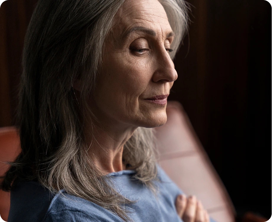 Older woman with gray hair in profile, looking downward thoughtfully