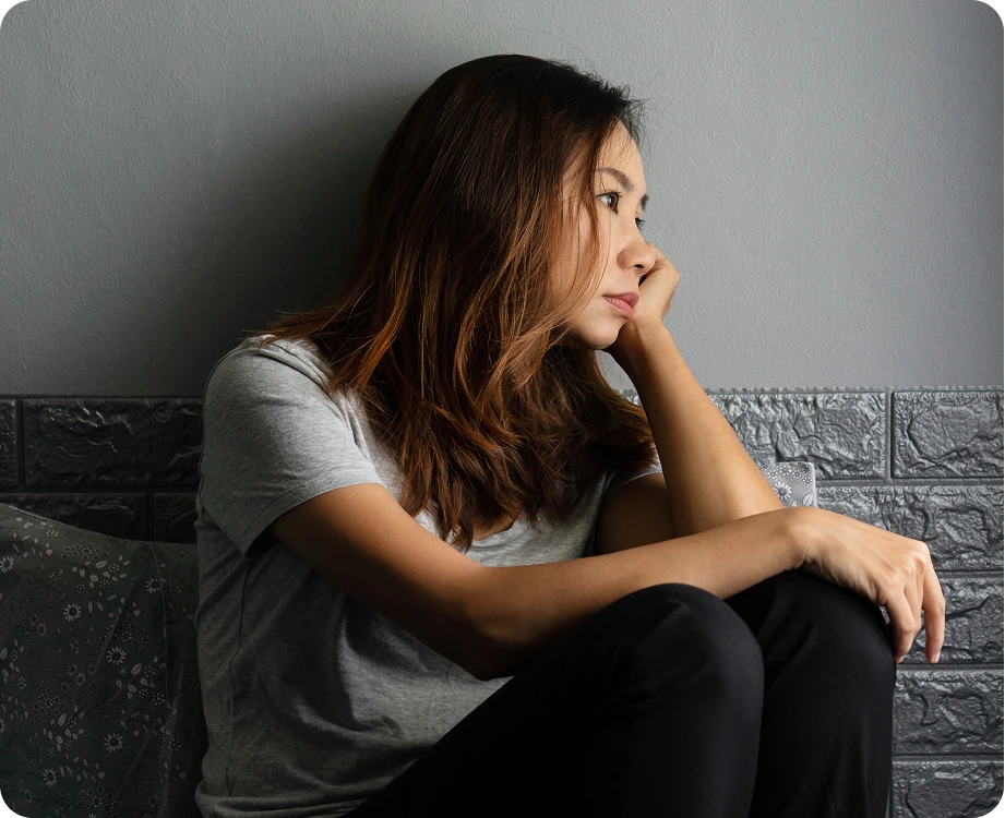Woman sitting against brick wall with hand to face, looking contemplative