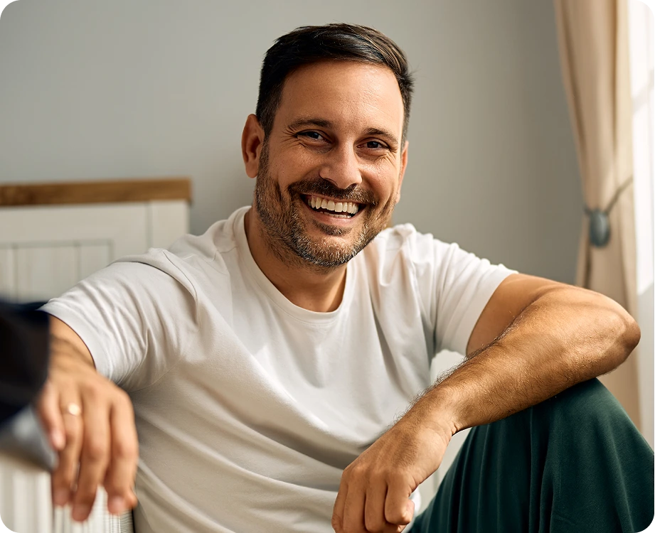 Man in white t-shirt smiling while seated indoors