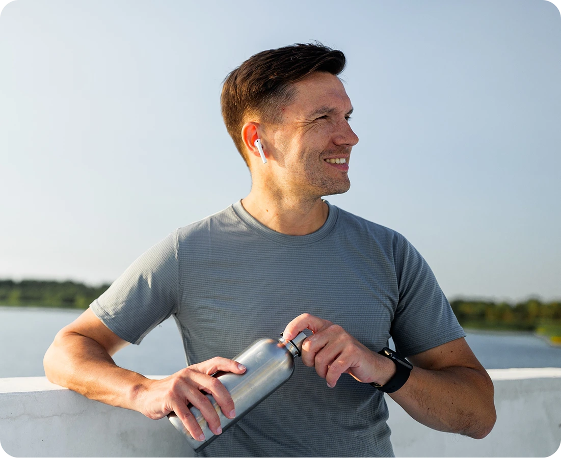 Man smiling while holding water bottle outdoors by water