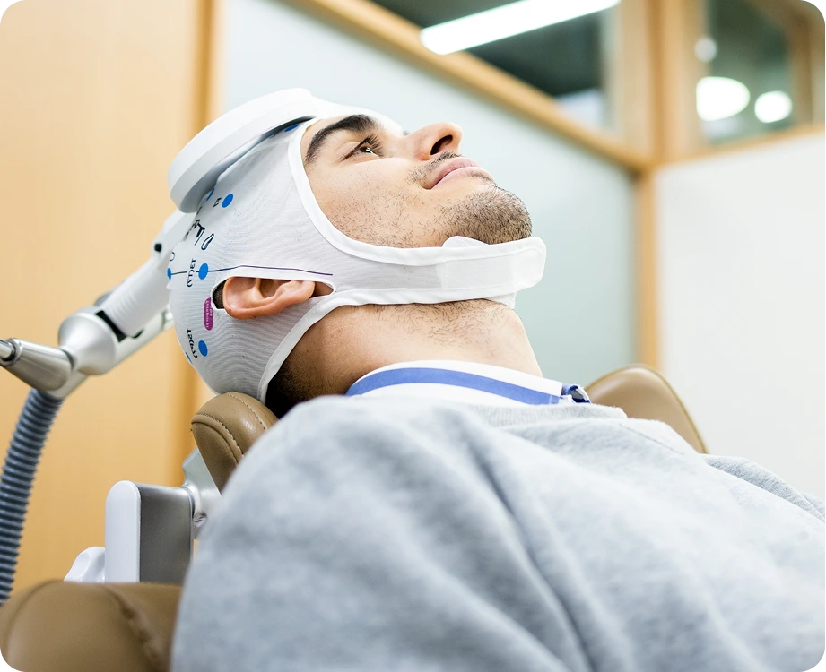 Patient receiving transcranial magnetic stimulation treatment with white coil device positioned on head