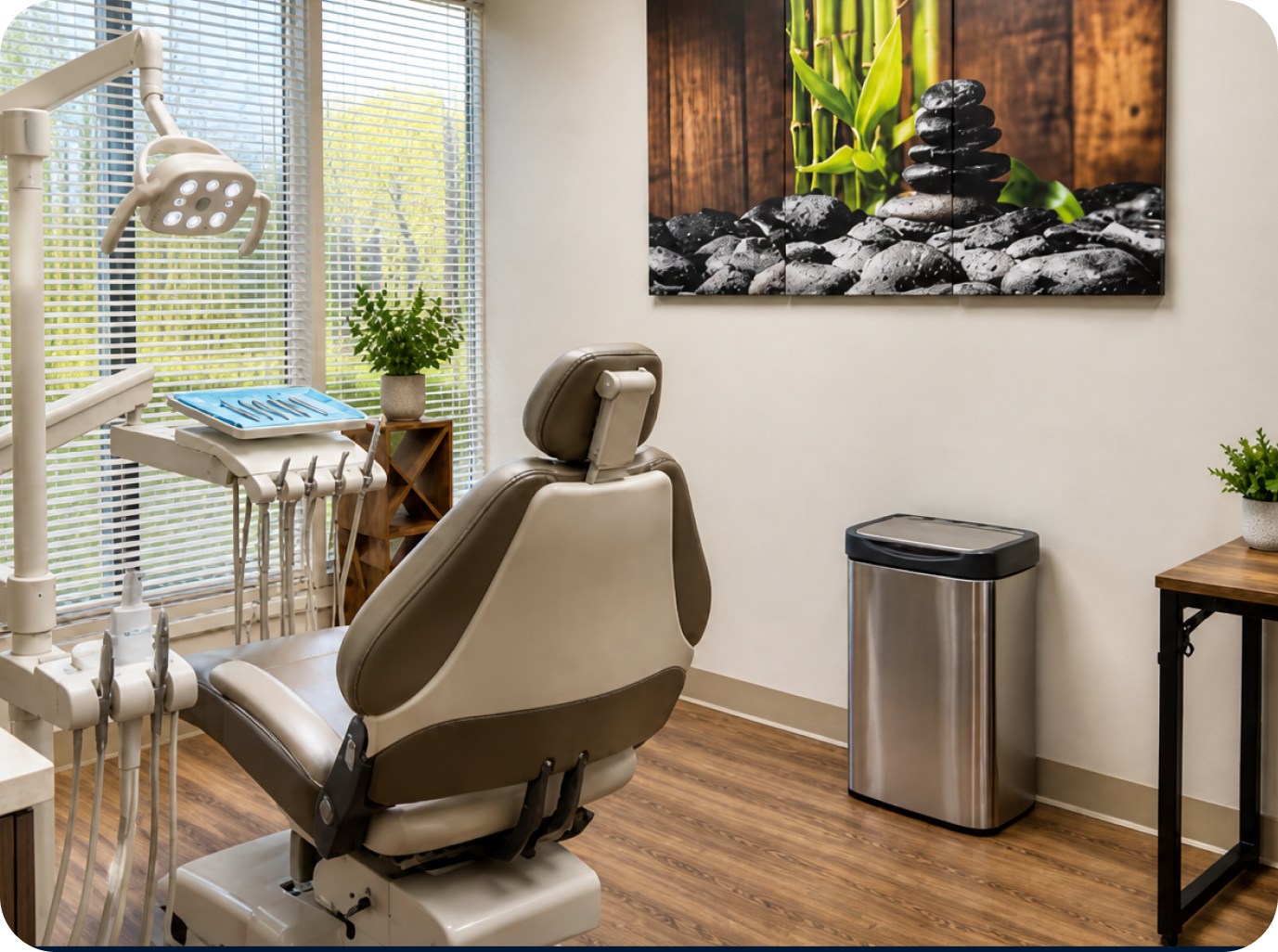 Modern dental treatment room with beige patient chair, overhead light, instrument tray, and calming zen wall art with stacked stones and green plant
