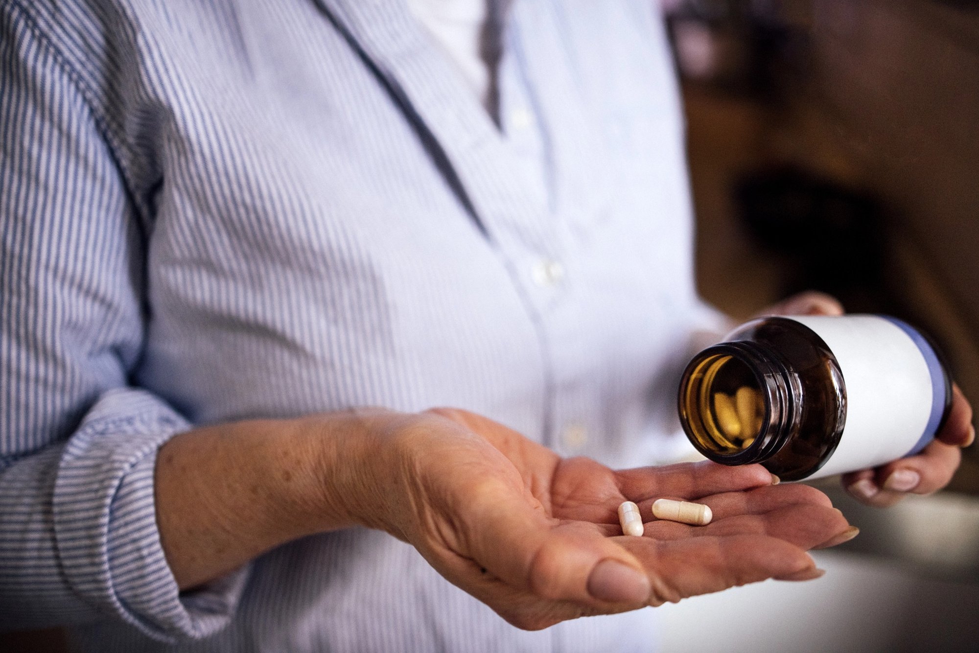 Capsules poured from an amber prescription bottle into a patient's hand